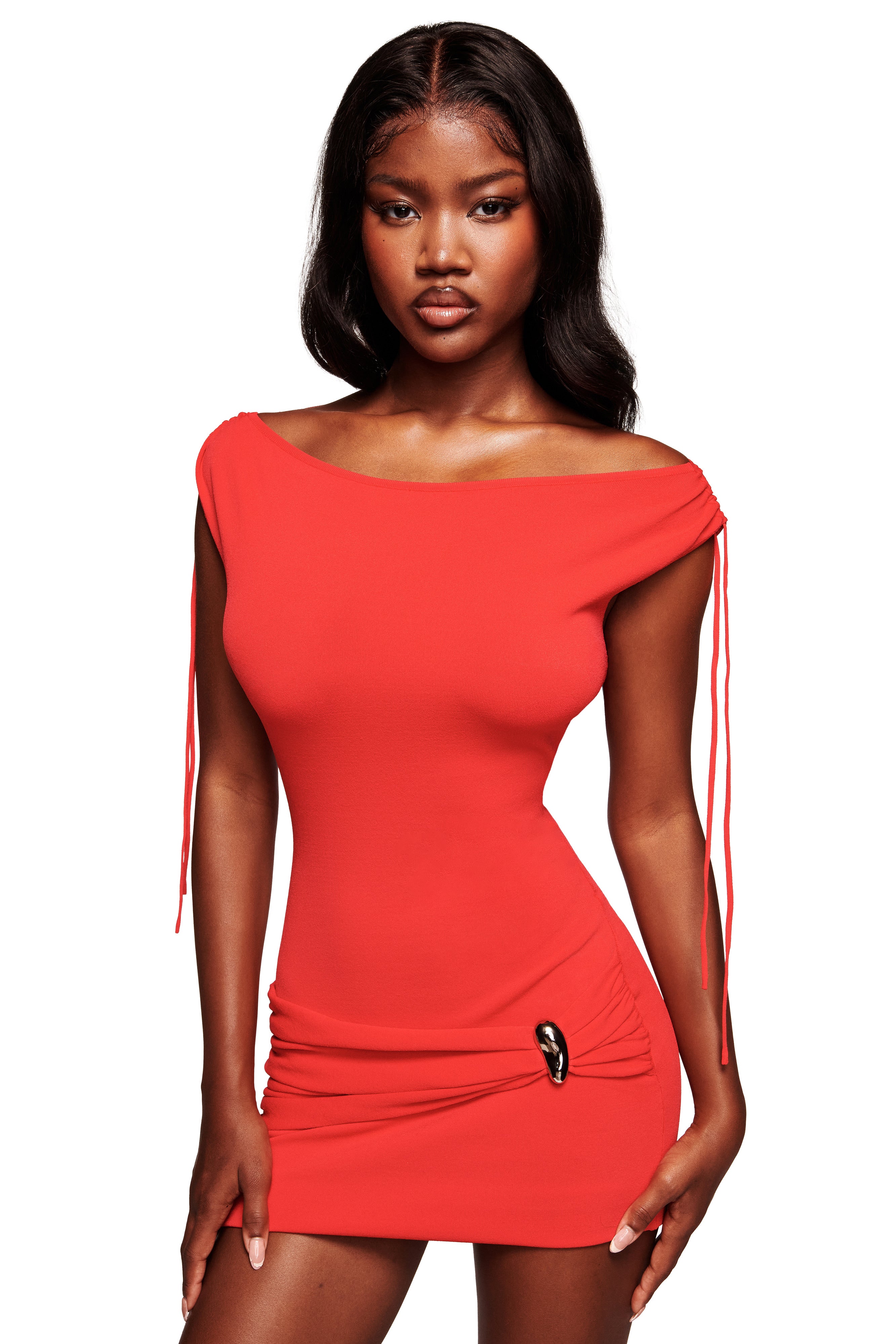 A woman models the I.AM.GIA SUGAR MINI DRESS in red, featuring a form-fitting silhouette, cap sleeves, and side tie accents. The ruched hips enhance her shape as she poses confidently against a white background.
