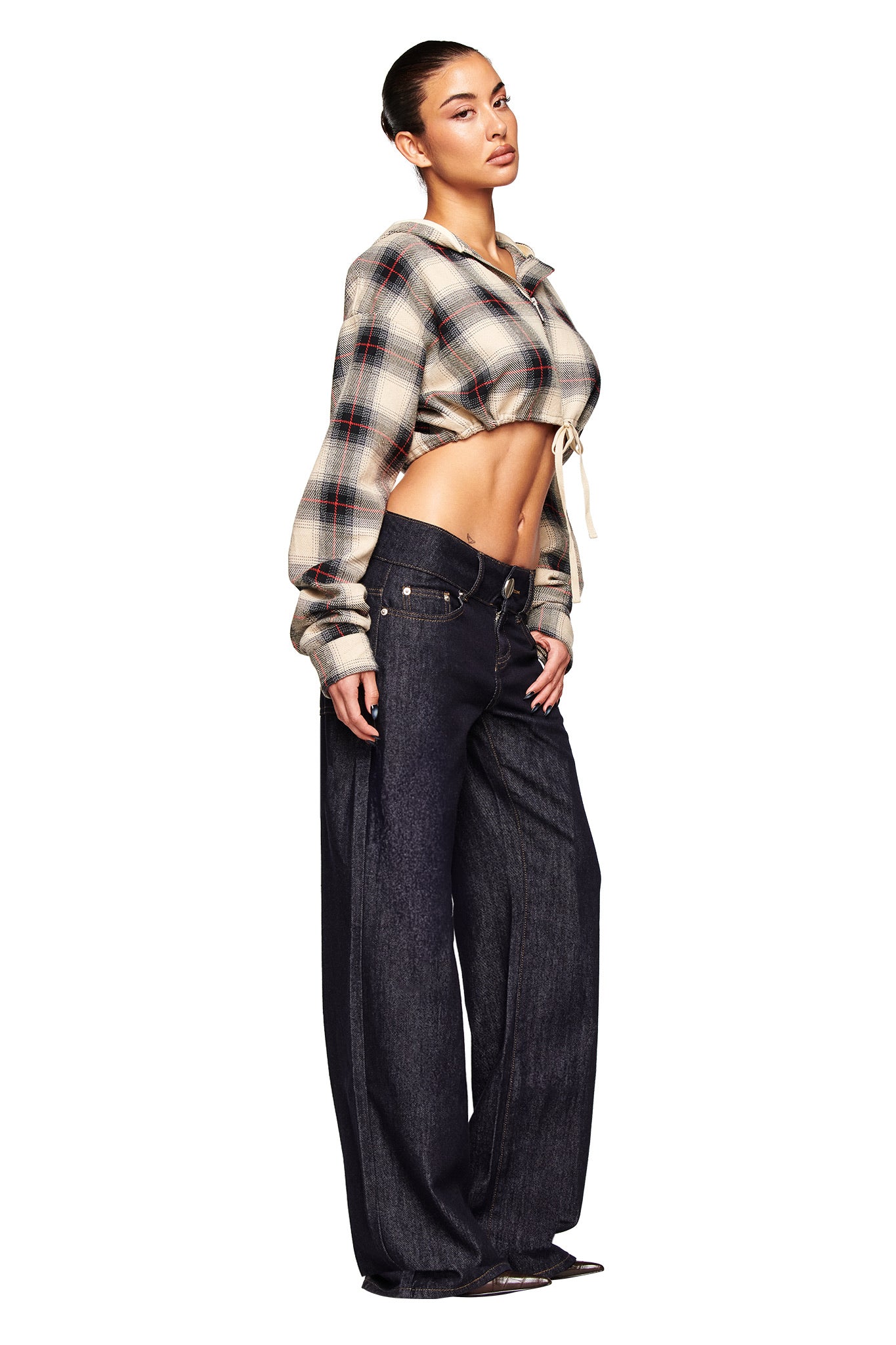 A woman stands against a white background wearing the I.AM.GIA TIFF JACKET in grey plaid, styled cropped to reveal her midriff, paired with low-rise, wide-leg dark jeans. Her hair is tied back and she gazes confidently to the side.