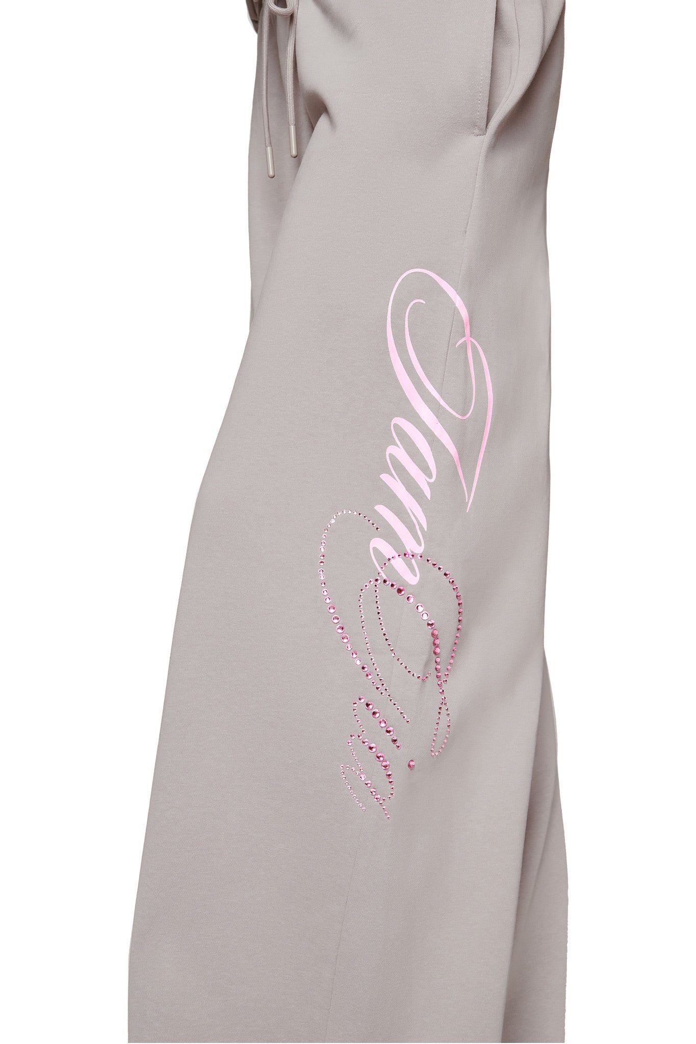 Close-up of KADE PANT - GREY by I.AM.GIA, a beige low-rise baggy pant featuring “Amour” in pink rhinestones with a pink heart outline above the script.