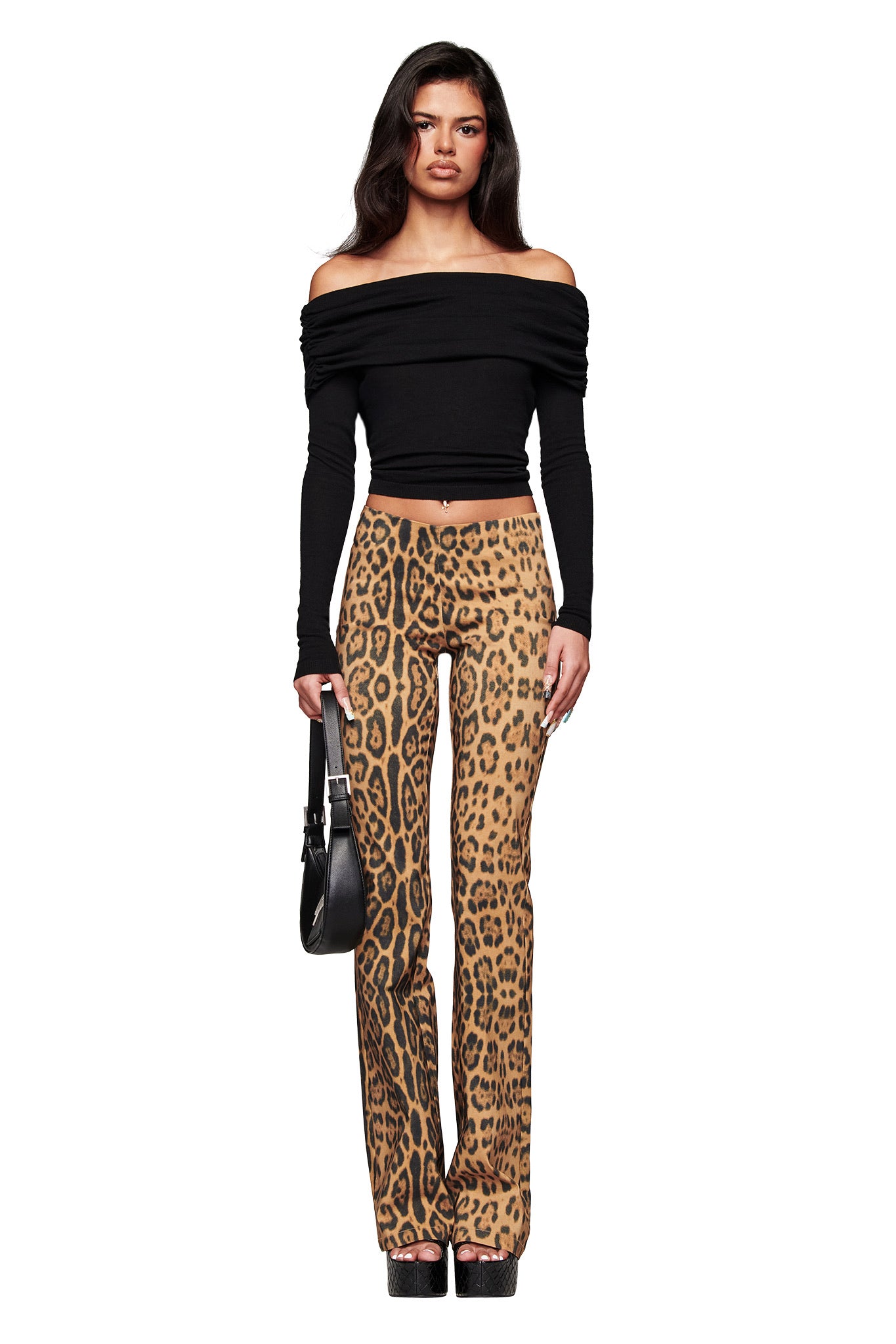 A woman faces forward against a white background, wearing the I.AM.GIA VEYRA LONG SLEEVE TOP in black, high-waisted leopard print pants, black platform shoes, and holding a black handbag.