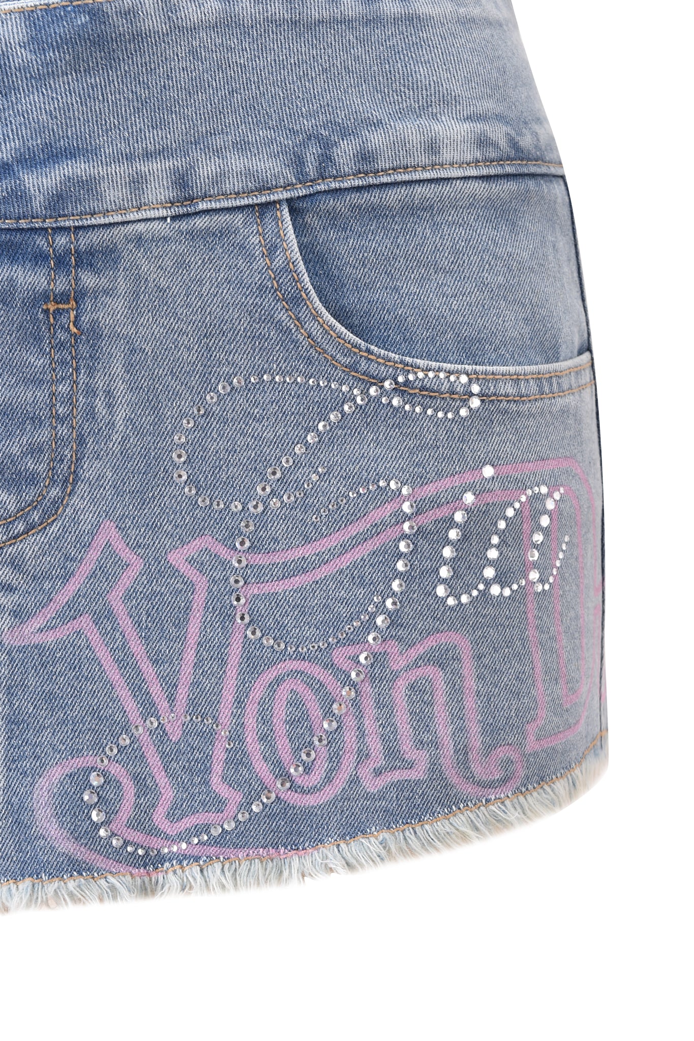 Close-up of the I.AM.GIA X VON DUTCH Syndra light wash denim mini skort, featuring a low rise waist, pink "Von Dutch" lettering, rhinestone accents, frayed hem, and a partial front pocket—an eye-catching collab piece by I.AM.GIA.