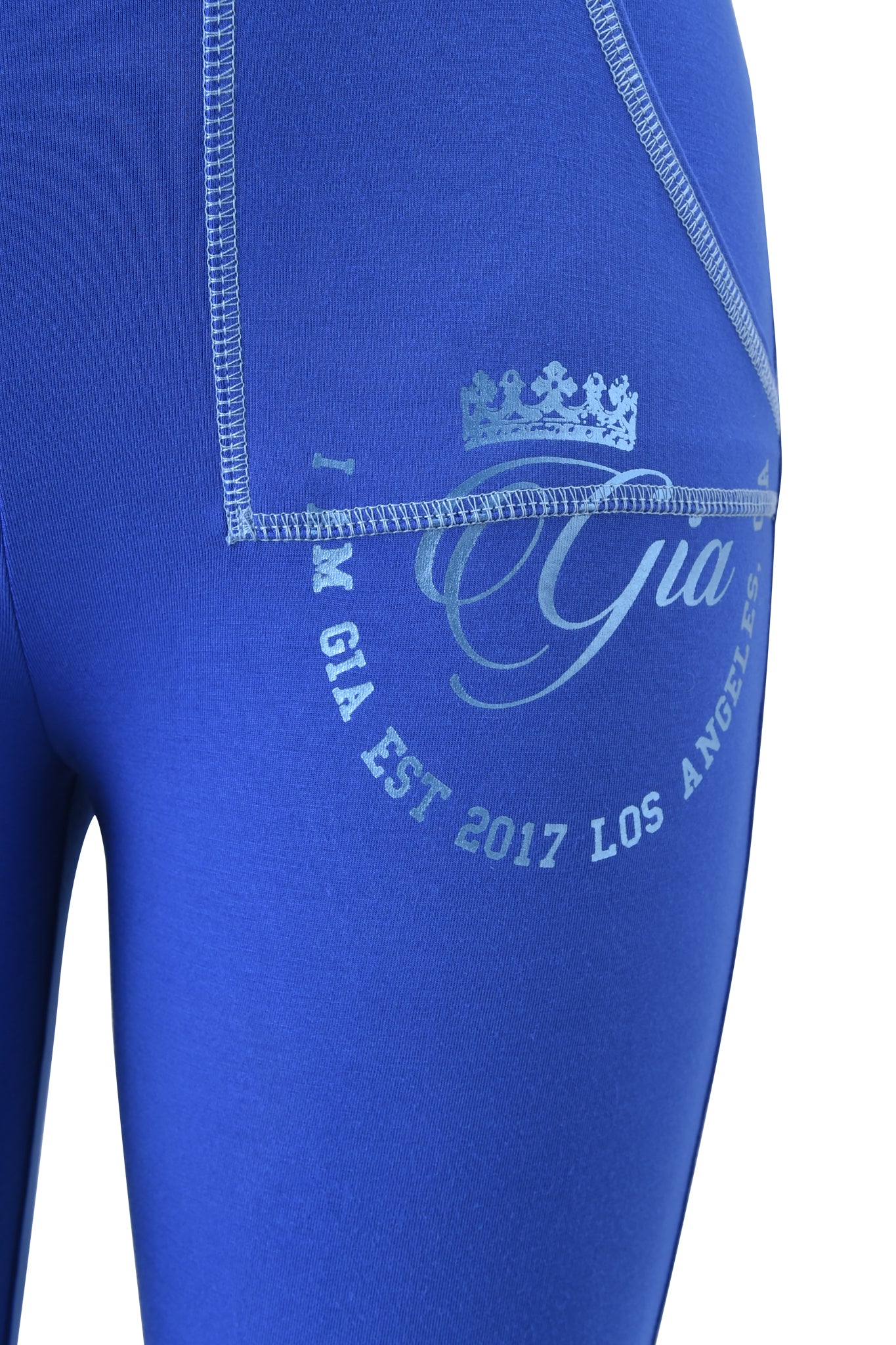 Close-up of a person wearing the I.AM.GIA BLARE FORM POCKET TRACKPANT - COBALT FOIL featuring white stitching and a "Gia EST 2017 LOS ANGELES" print with a crown graphic near the hip.
