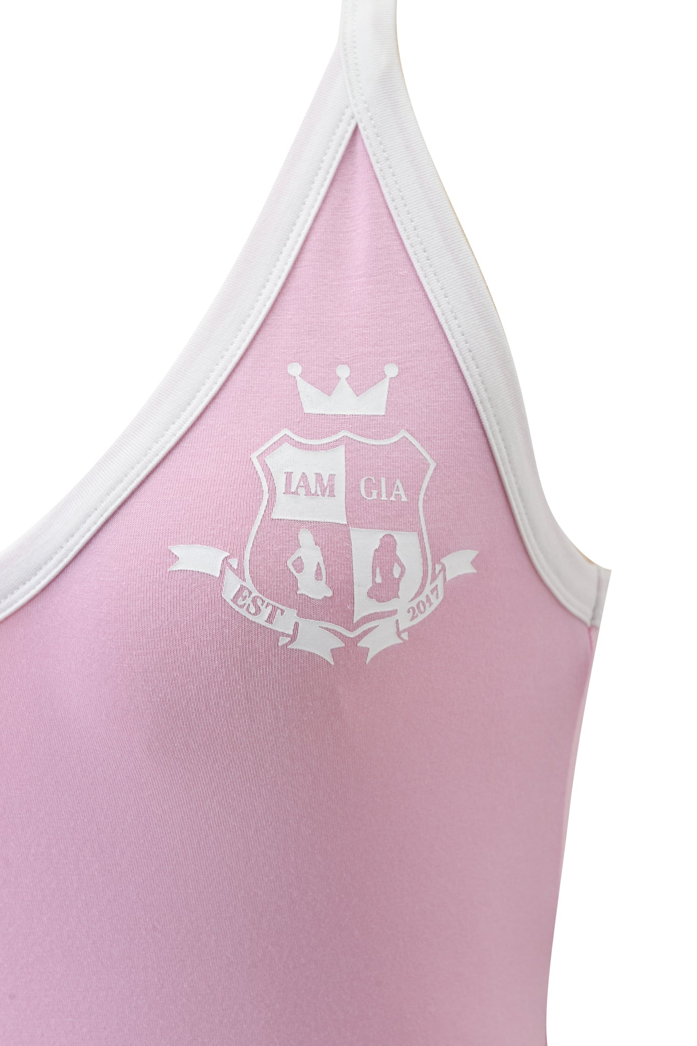 Close-up of the BLARE V-NECK TANK in baby pink and white by I.AM.GIA, featuring a soft viscose fabric, white trim, and a printed crest with crown, "IAM GIA," two seated figures, and "EST 2017" on a ribbon banner.