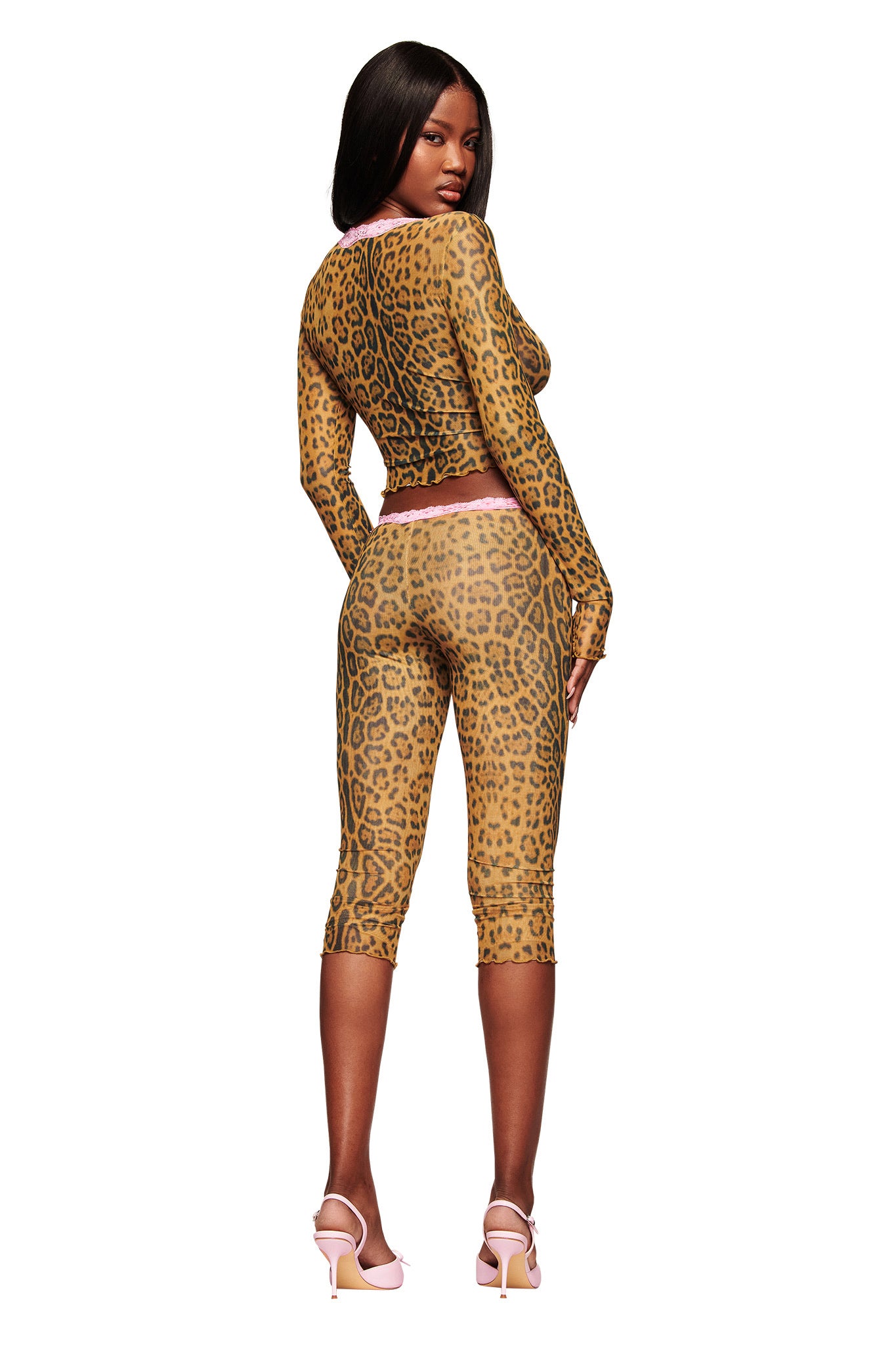 A woman faces away, turning her head to look back. She wears the I.AM.GIA TASHI TOP - PANTHERA with matching capri pants and pale pink heels against a white background.