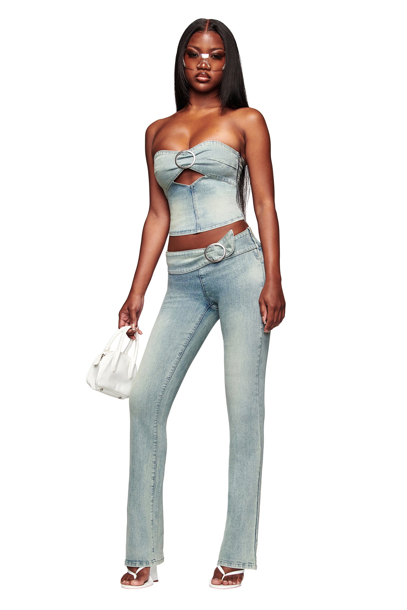 A woman wears the I.AM.GIA JENN DENIM BOOB TUBE in blue with matching high-waisted jeans featuring a belt ring, paired with heeled sandals and a small white purse, highlighting the bodycon fit of her outfit.