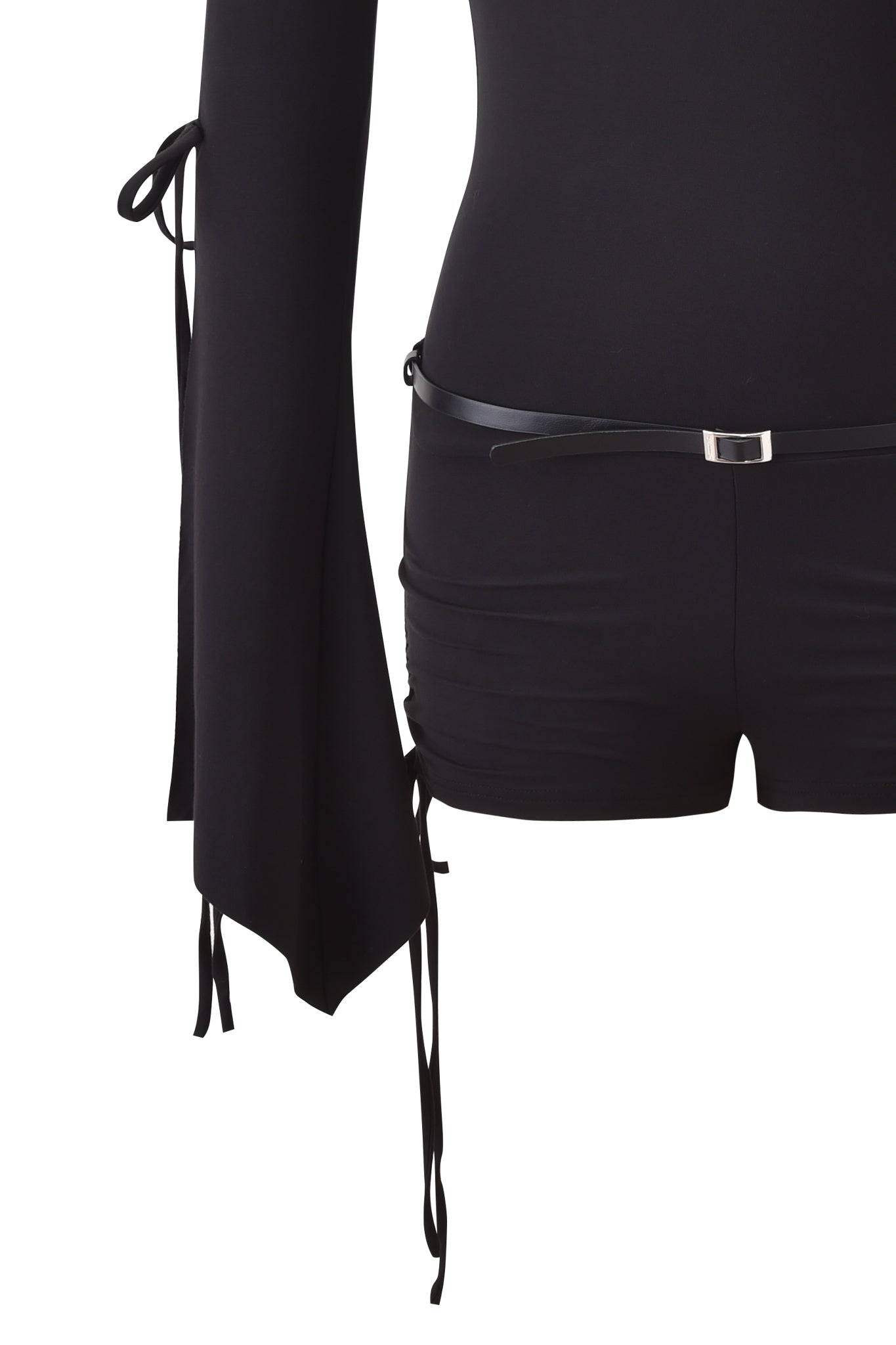 A person wears the I.AM.GIA SAPHY PLAYSUIT in black, a long-sleeve off-shoulder design with flared sleeves and tie details, styled with a thin black belt featuring a silver buckle. The image is cropped from the chest down.