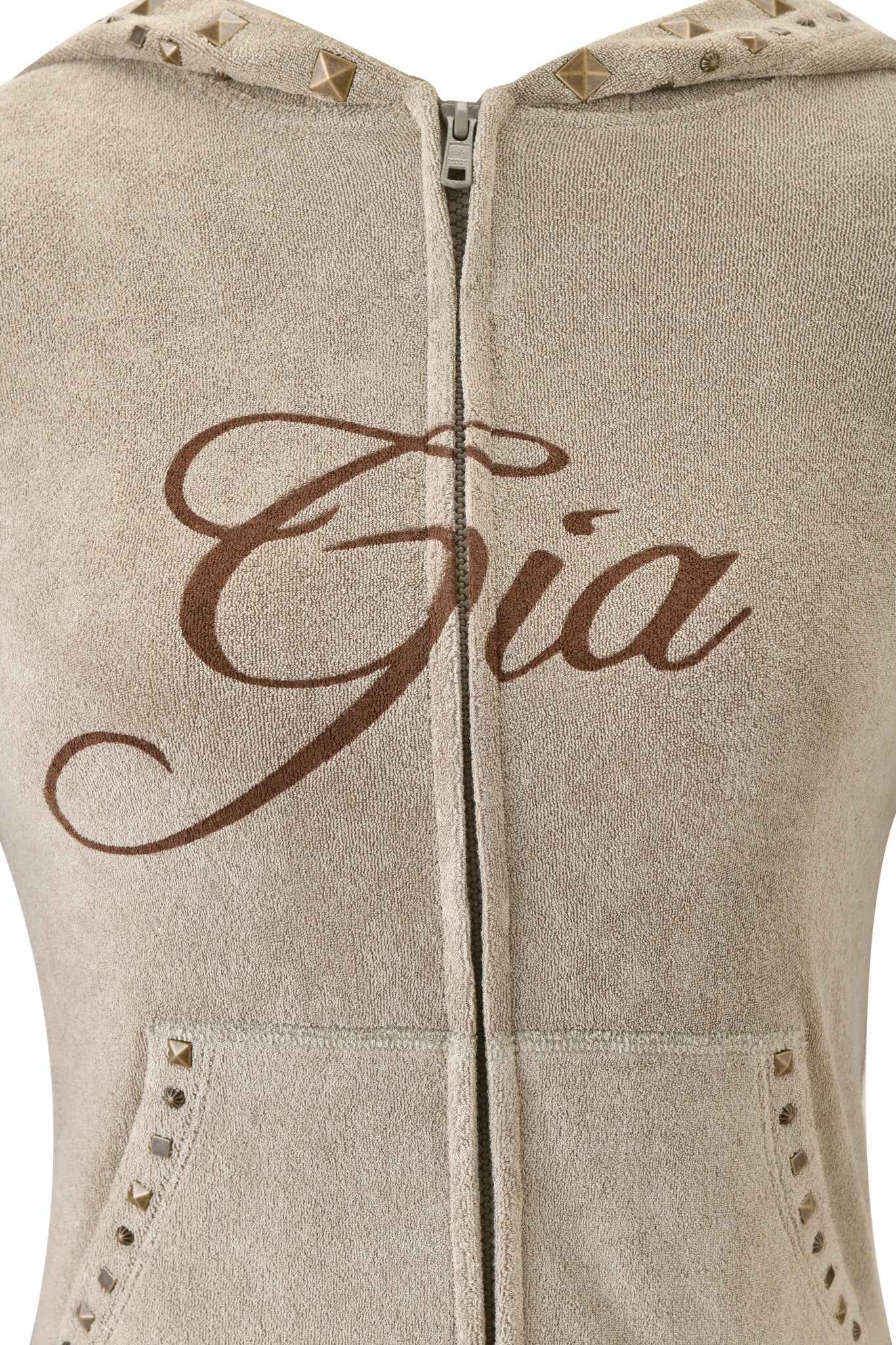 Close-up of the I.AM.GIA BLARE STUDDED TERRY HOODIE in Stone, featuring metallic studs on the hood and pockets. "Gia" is printed in bold brown cursive across the chest, adding standout style to this beige terry cloth hoodie.