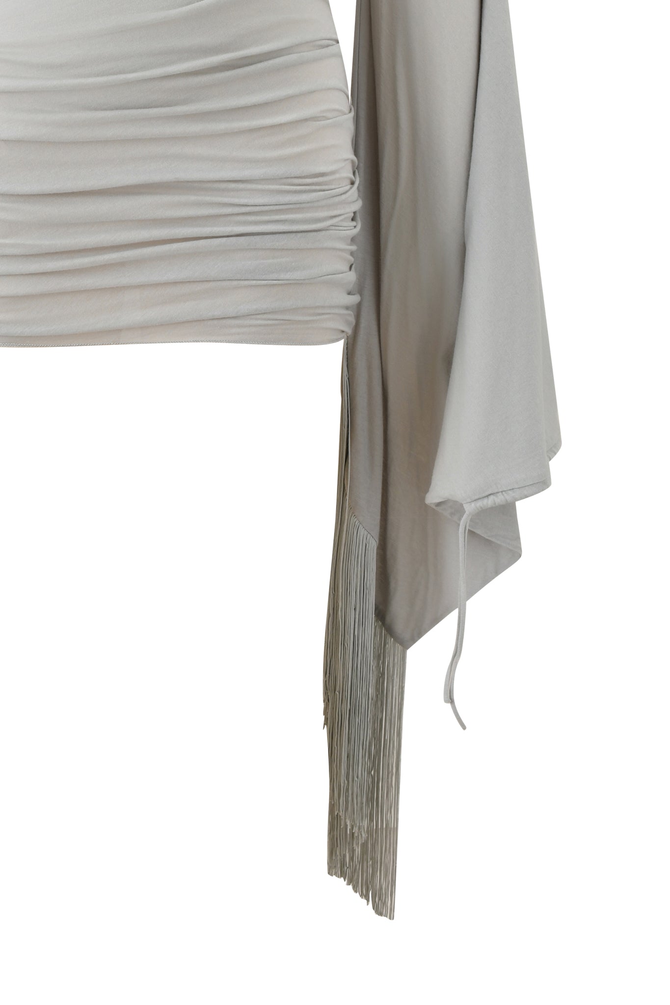 A close-up of the I.AM.GIA LUMA MINI DRESS - GREY, featuring light gray cotton jersey, ruched fabric, a long wide sleeve, and fringe detailing at the edge. The soft material drapes for a chic, modern appearance.