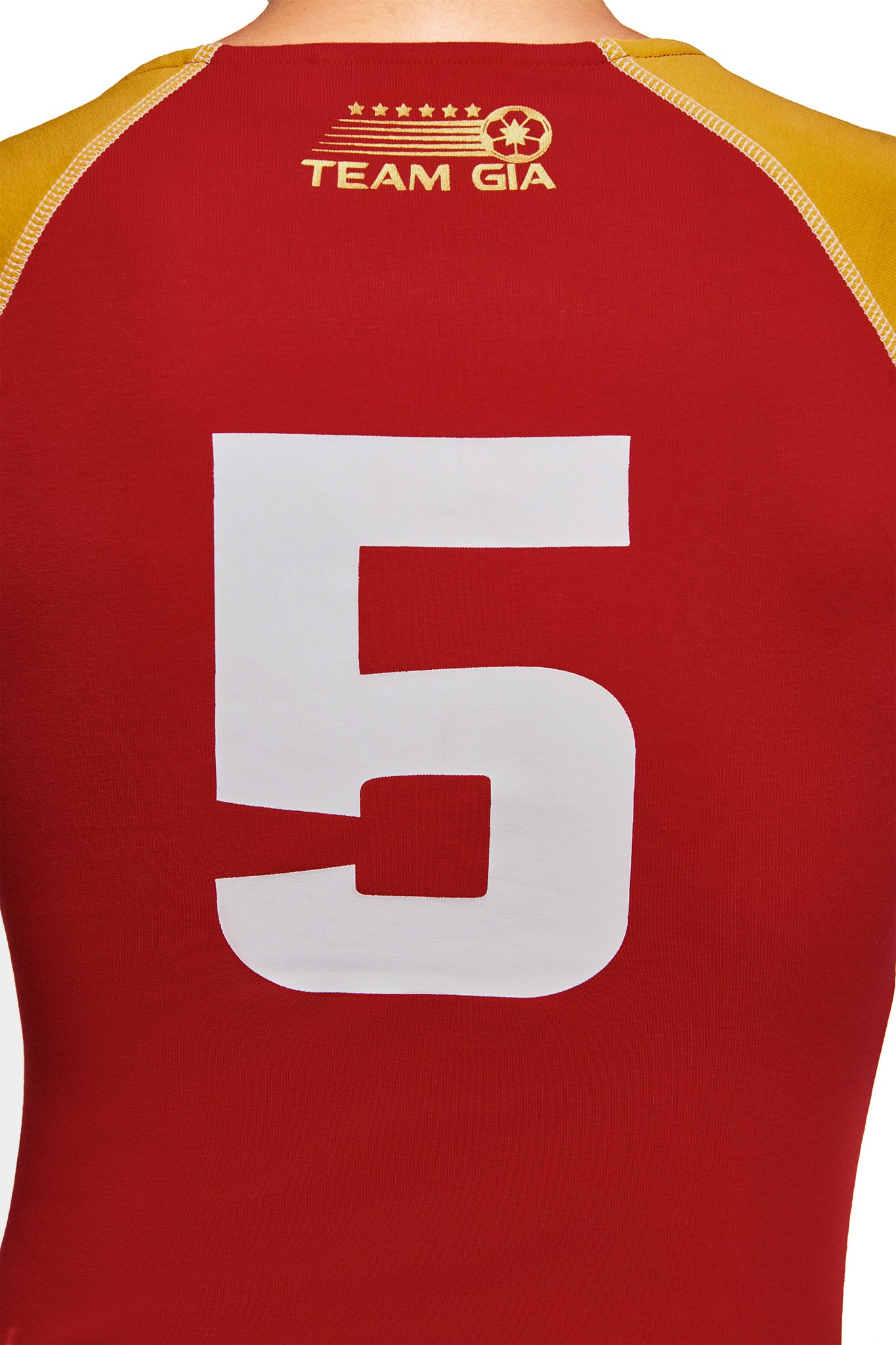 The back of the I.AM.GIA NOVIA Lace-Up T-Shirt and Headband in red shows yellow shoulders, a large white number 5, “TEAM GIA” with stars and a clover emblem, plus subtle I.AM.GIA branding above.
