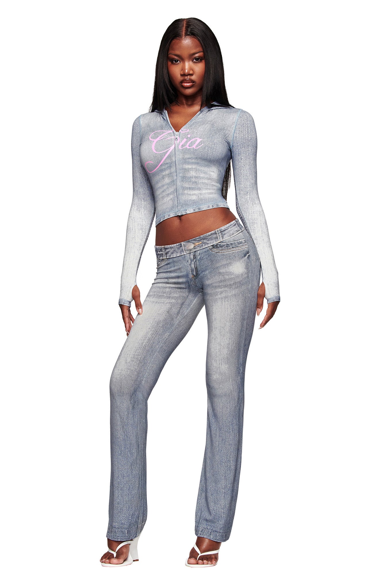 A woman stands confidently in the I.AM.GIA BLARE HOODIE - DENIM TROMPE L'OEIL, her long straight hair and open-toe heels reflecting iconic I.AM.GIA style.