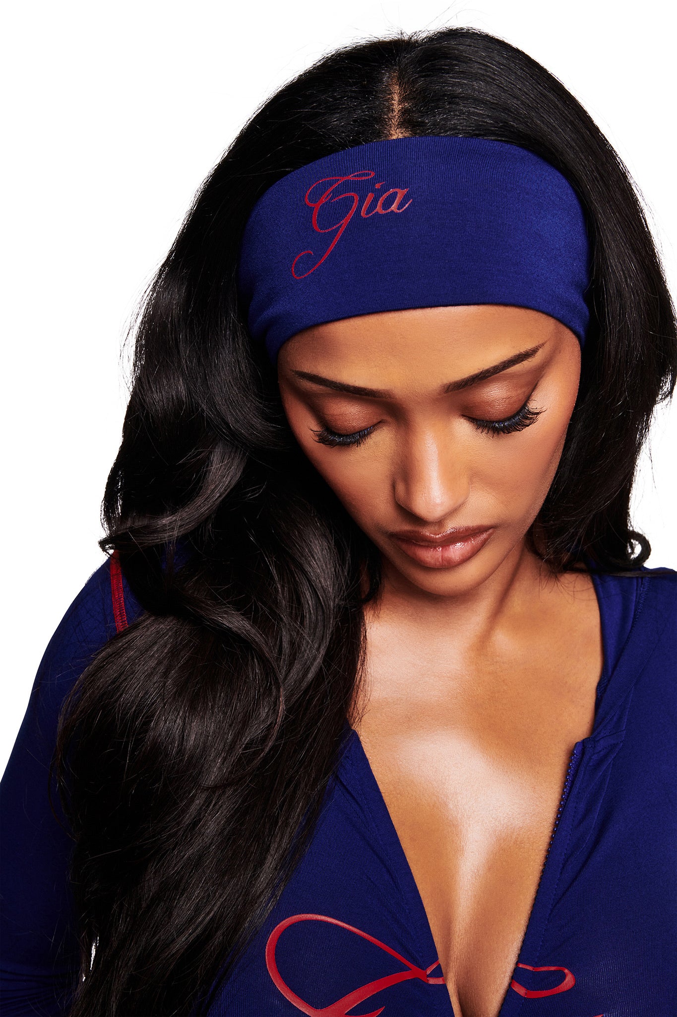 A woman with long black hair looks down, wearing the I.AM.GIA BLARE SPORT HEADBAND in navy and a matching blue zip-up top.