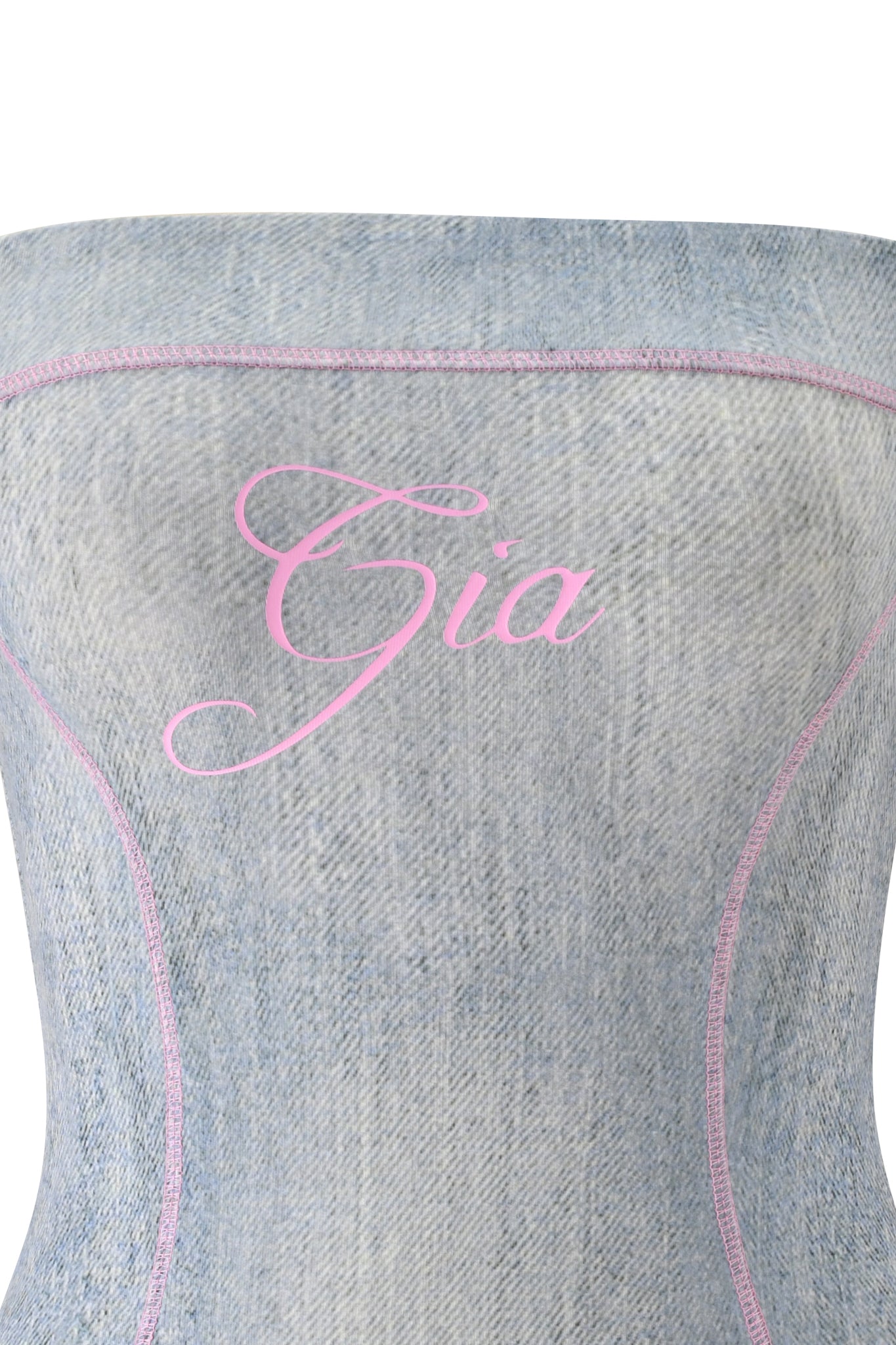 A close-up of the I.AM.GIA BLARE TUBE MINI DRESS - DENIM TROMPE L'OEIL, a strapless light denim corset-style dress featuring pink stitching and "Gia" printed in pink cursive across the chest.