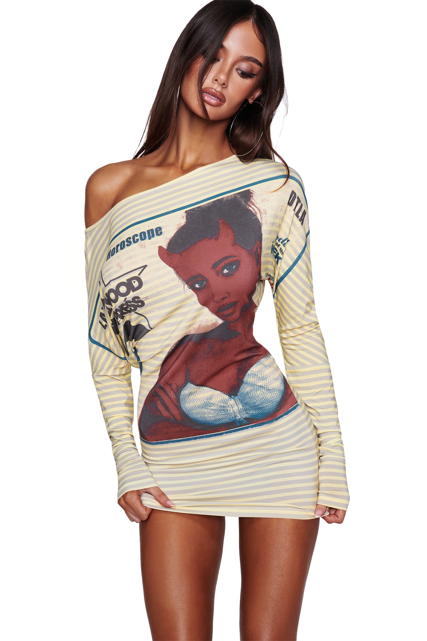 A woman wears the I.AM.GIA T-REX GISELLE OFF SHOULDER MINI DRESS in yellow—an edgy off-shoulder, long-sleeve batwing dress featuring bold stripes and a striking front graphic of a red-skinned cartoon woman with horns, accompanied by the words “Horoscope” and “Blood Drip,” all set against a white background.