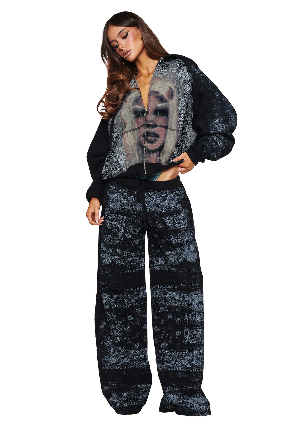 A woman stands against a white background wearing the I.AM.GIA T-REX ZIP THRU HOODIE in Black Bandana with matching pants, featuring a graphic image of Marilyn Monroe printed on the front of the oversized zip-up hoodie.