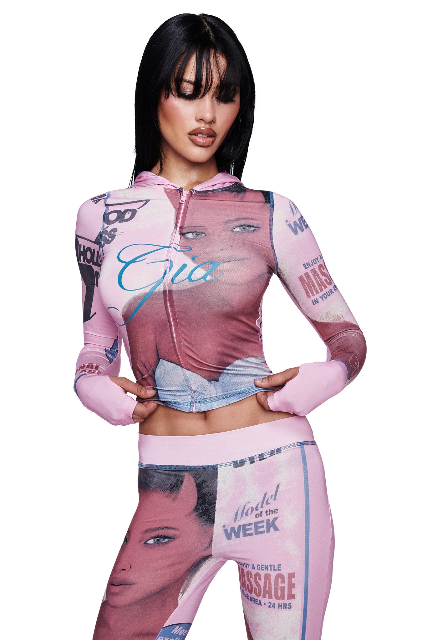 A woman poses in the I.AM.GIA T-REX BLARE HOODIE - PINK and matching leggings, both featuring vintage magazine covers, bold headlines, and a large portrait graphic. She wears her long black hair with bangs and stands confidently with her hands on her hips.