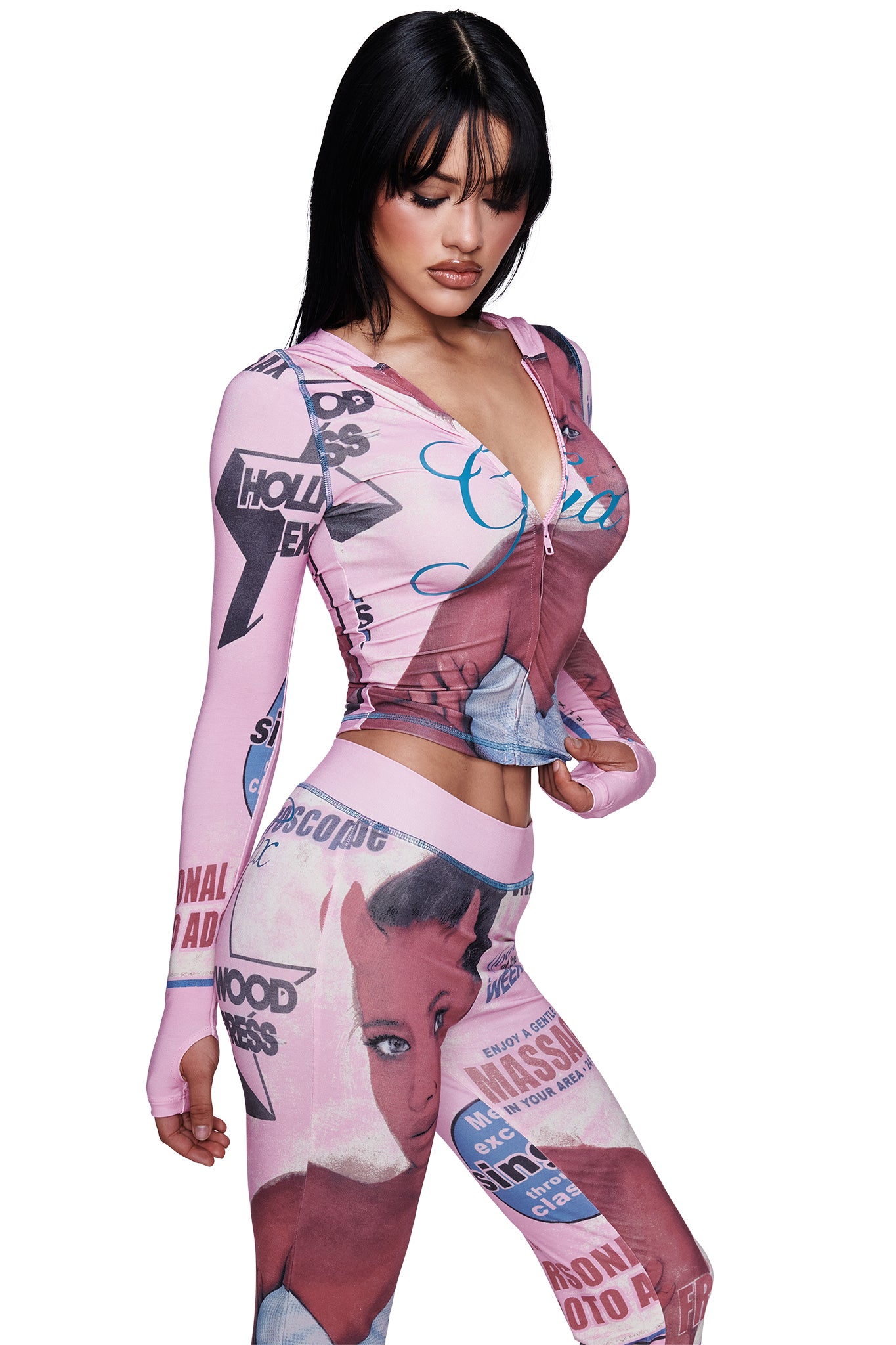A woman stands against a plain white background wearing the I.AM.GIA T-REX BLARE TRACKPANT in pink, a fitted style featuring bold, vintage-inspired graphics and the eye-catching T-REX pink print. She looks down with her hands near her waist, highlighting the pant’s wide elastic waistband designed for both comfort and style.