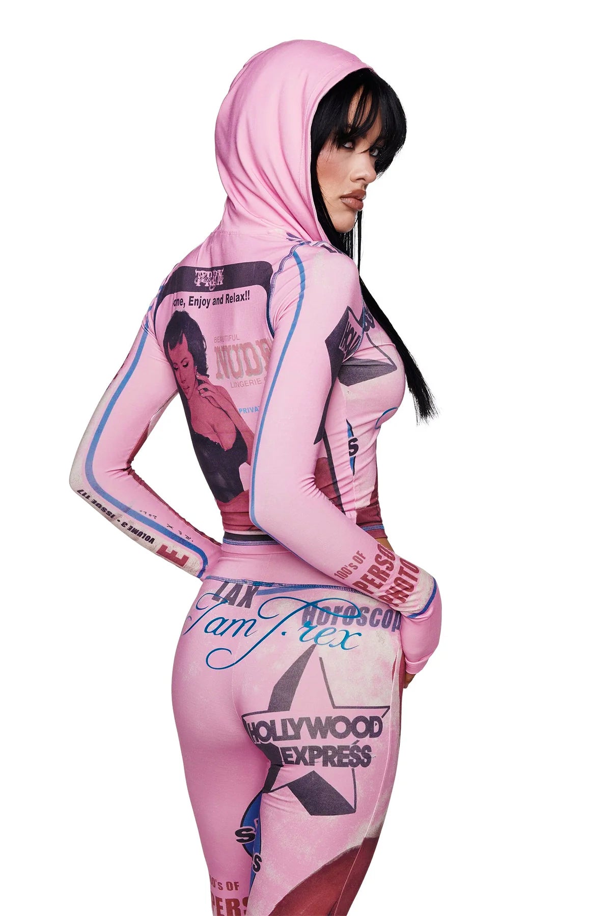 A woman dressed in the I.AM.GIA T-REX BLARE HOODIE in pink—featuring a form-fitting silhouette and vintage-inspired magazine print—poses with her body angled to the side, glancing back over her shoulder.