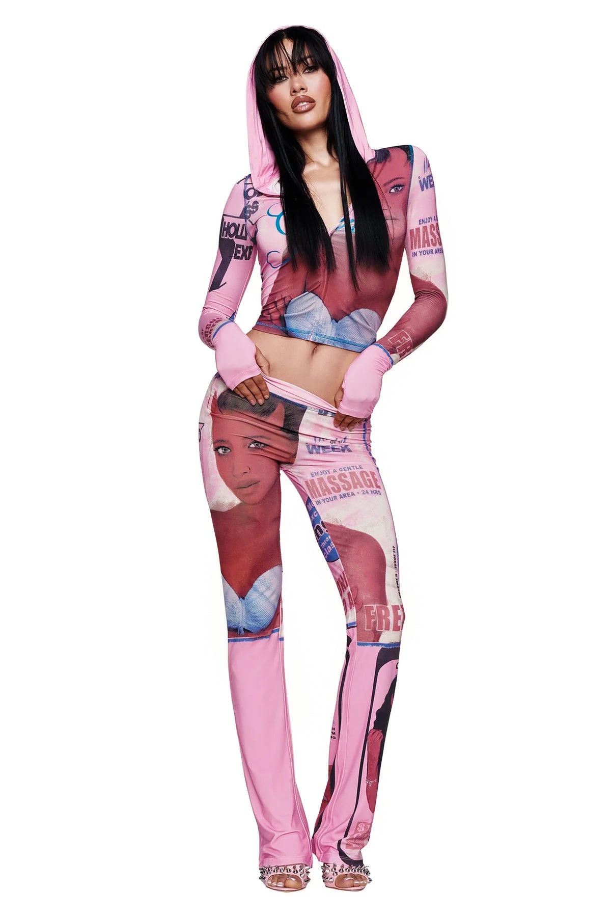 A woman poses wearing the I.AM.GIA T-REX BLARE HOODIE in pink along with matching pants, both showcasing bold, colorful graphic prints of a woman's face and text. The striking outfit is finished with fingerless gloves and high heels, all made from soft bamboo fabric for comfort and impact.