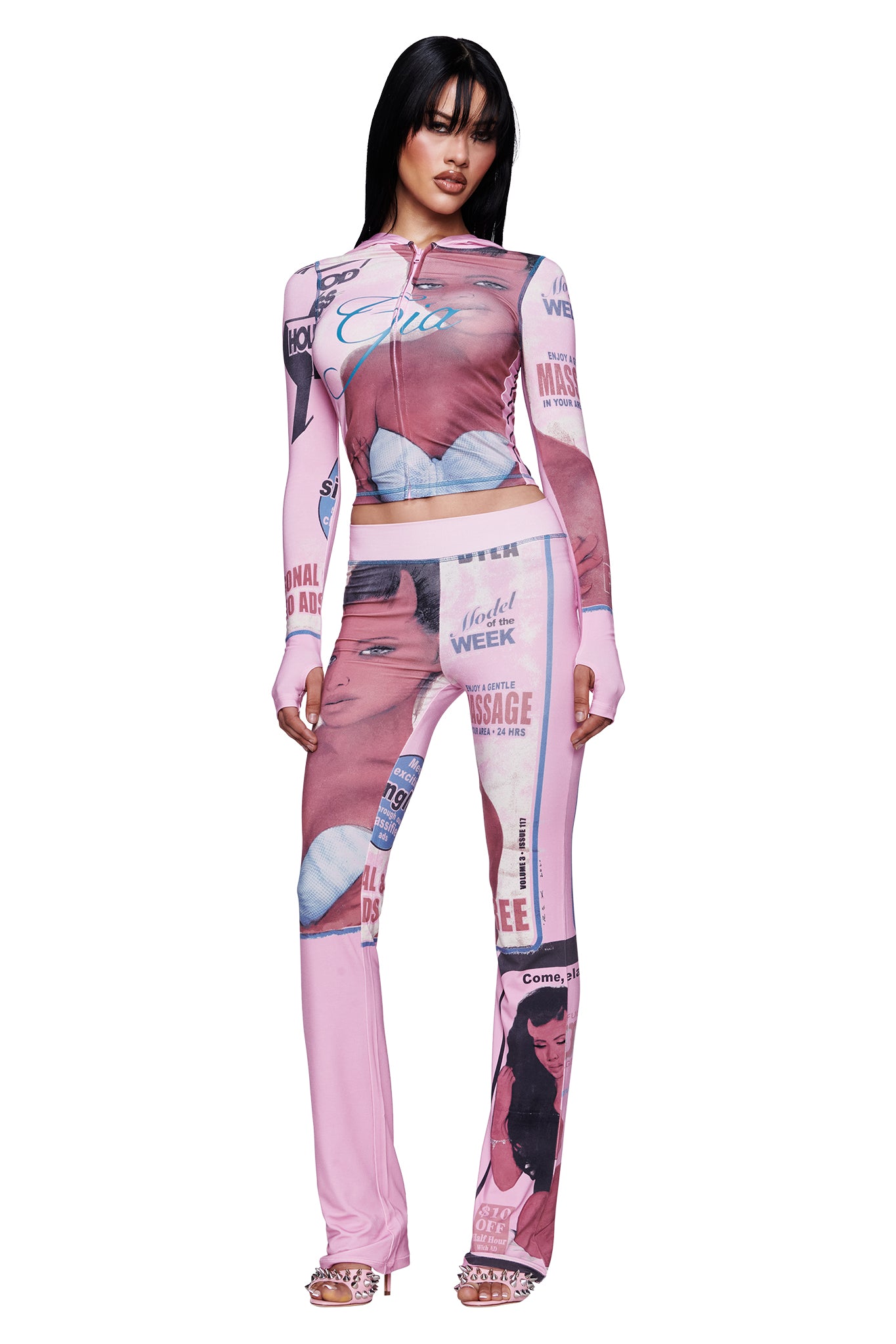 A woman wearing the I.AM.GIA T-REX BLARE HOODIE in pink, featuring fitted styling with graphic images and magazine-style headline prints, stands with her arms at her sides and looks forward.