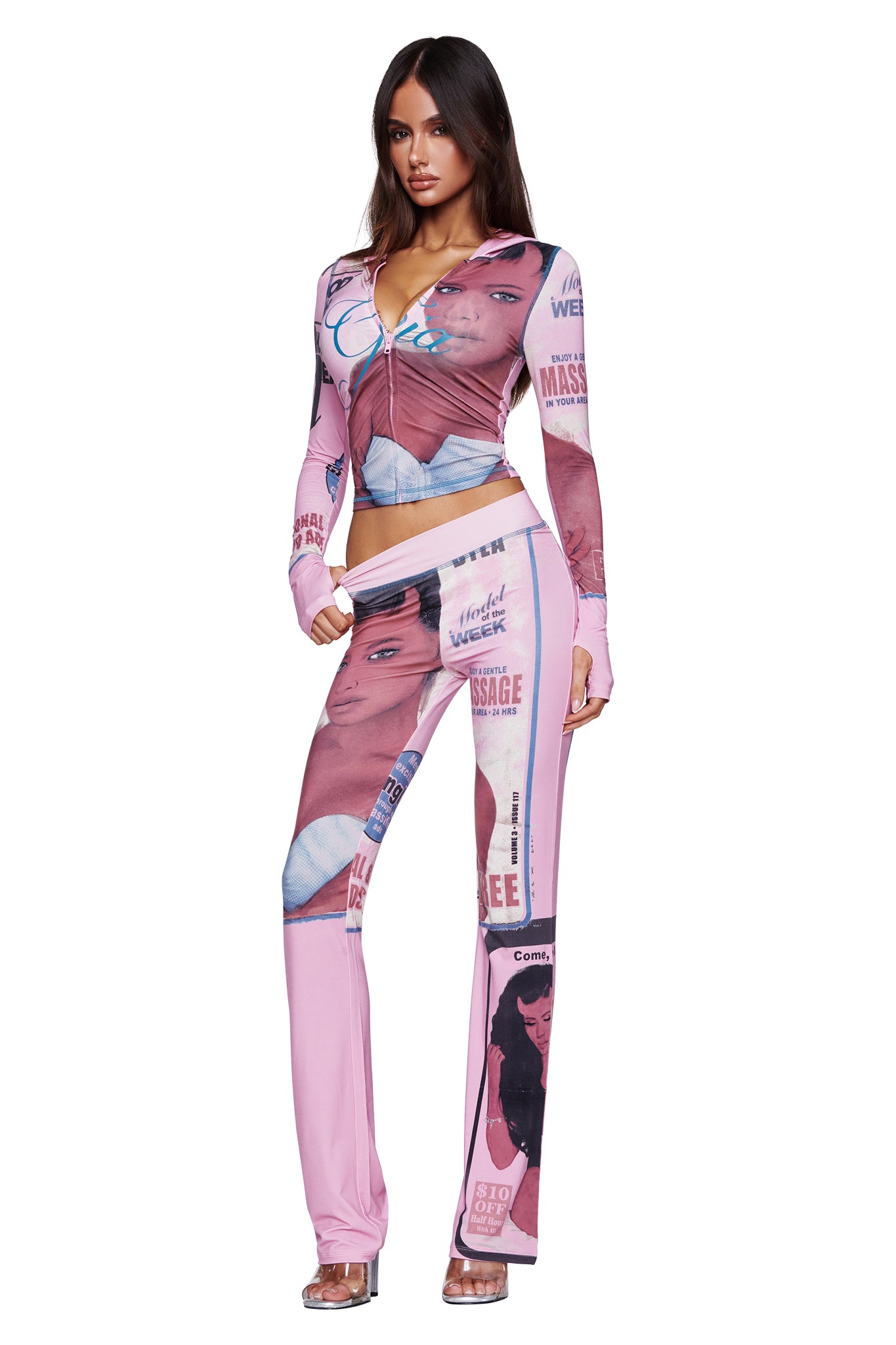A woman wears the I.AM.GIA T-REX BLARE HOODIE in pink, featuring a placement print and text. She stands facing forward in clear high-heeled shoes against a white background.