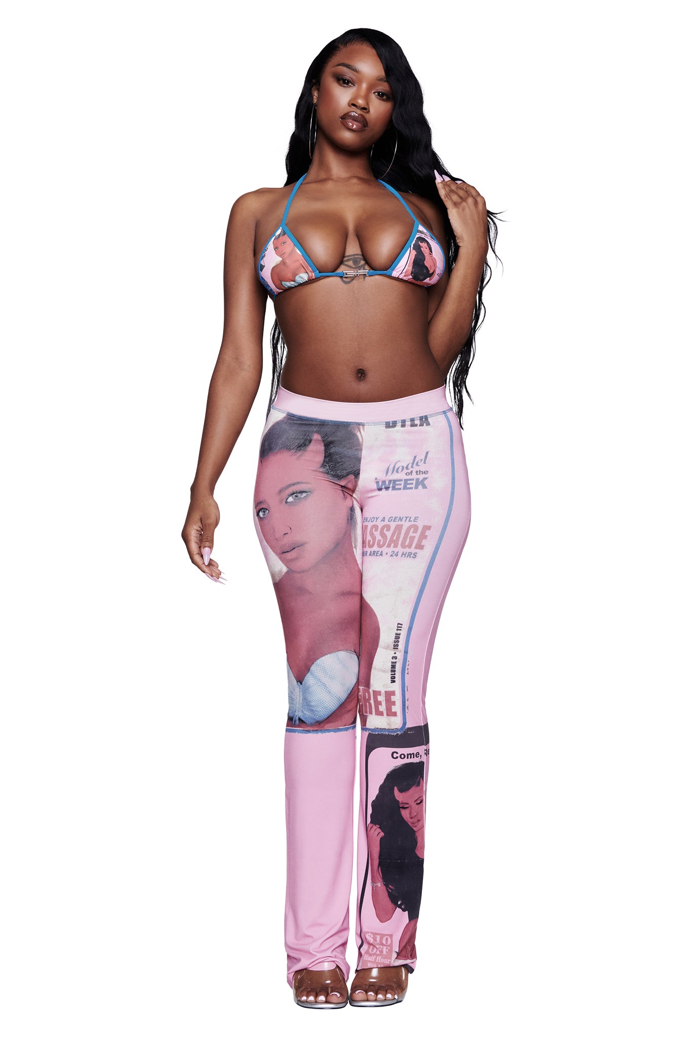 A woman poses confidently against a white background wearing a bikini top and the T-REX BLARE TRACKPANT - PINK by I.AM.GIA, which features illustrated women, magazine covers, and a wide elastic waistband.