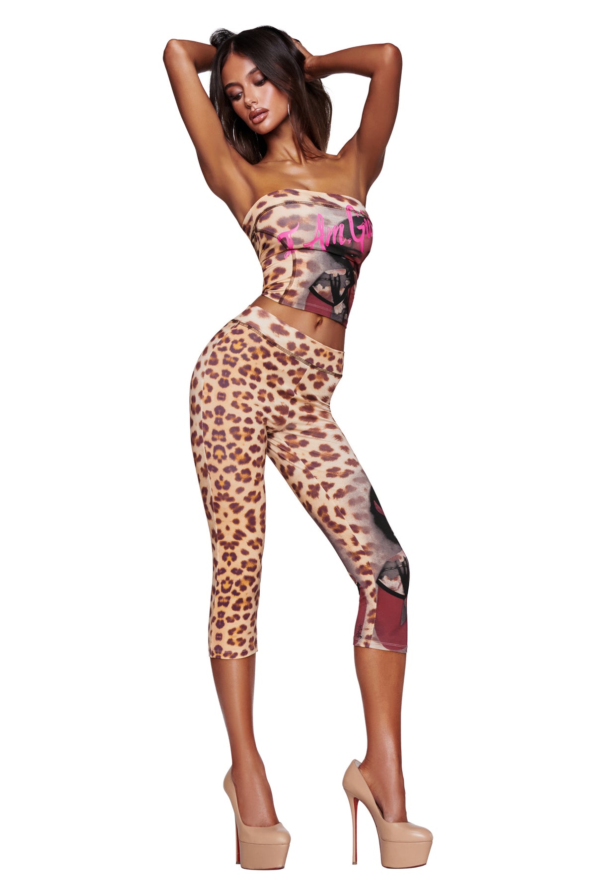A woman poses in the I.AM.GIA T-REX BLARE BOOB TUBE - WILD CARD and matching leggings with high nude heels, standing against a white background with her hands raised behind her head.