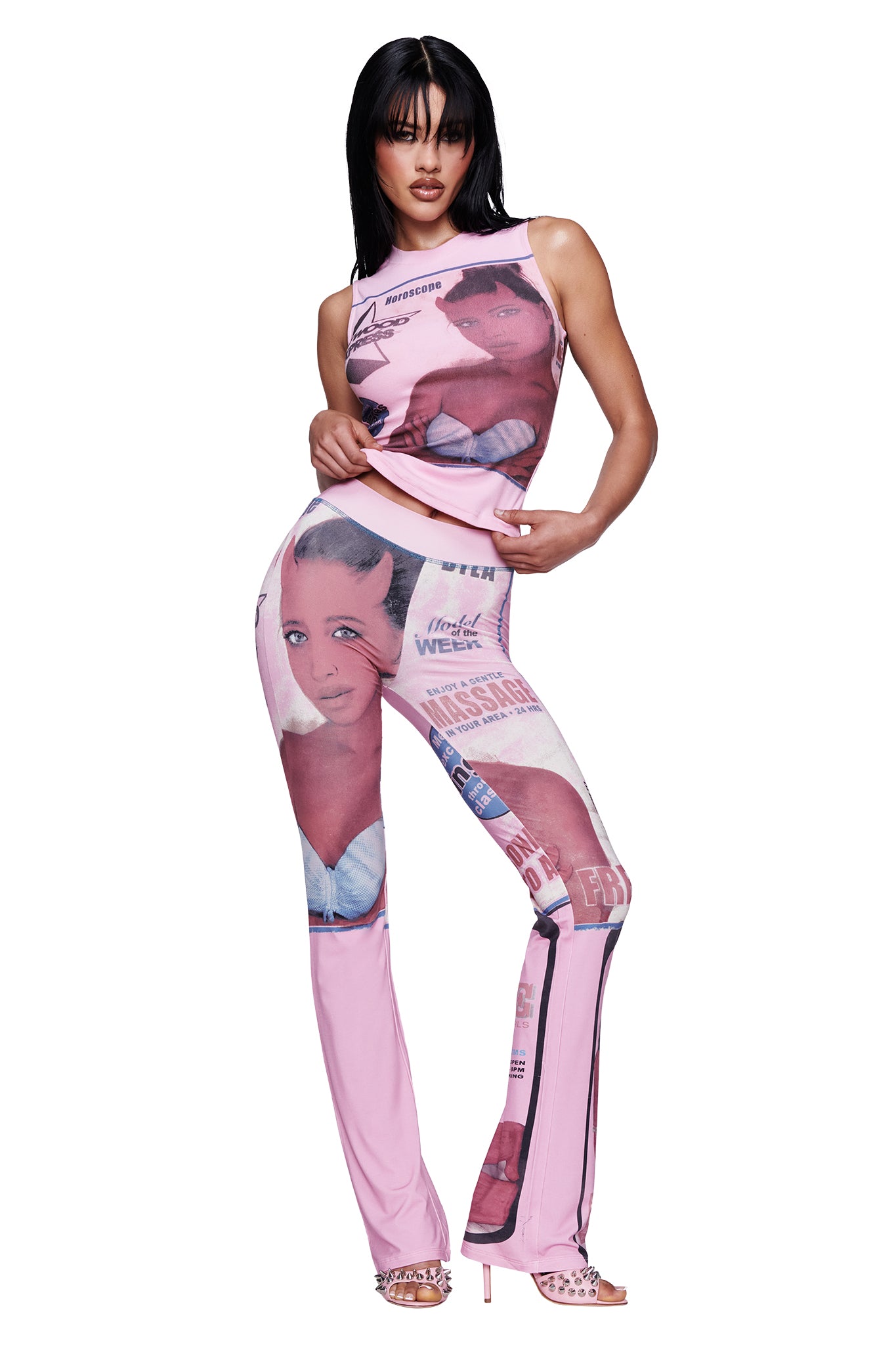 A woman poses against a white background wearing the I.AM.GIA T-REX COURTNEY TANK in pink with flared pants featuring a pink collage print of illustrated faces and text, styled with open-toe heels.