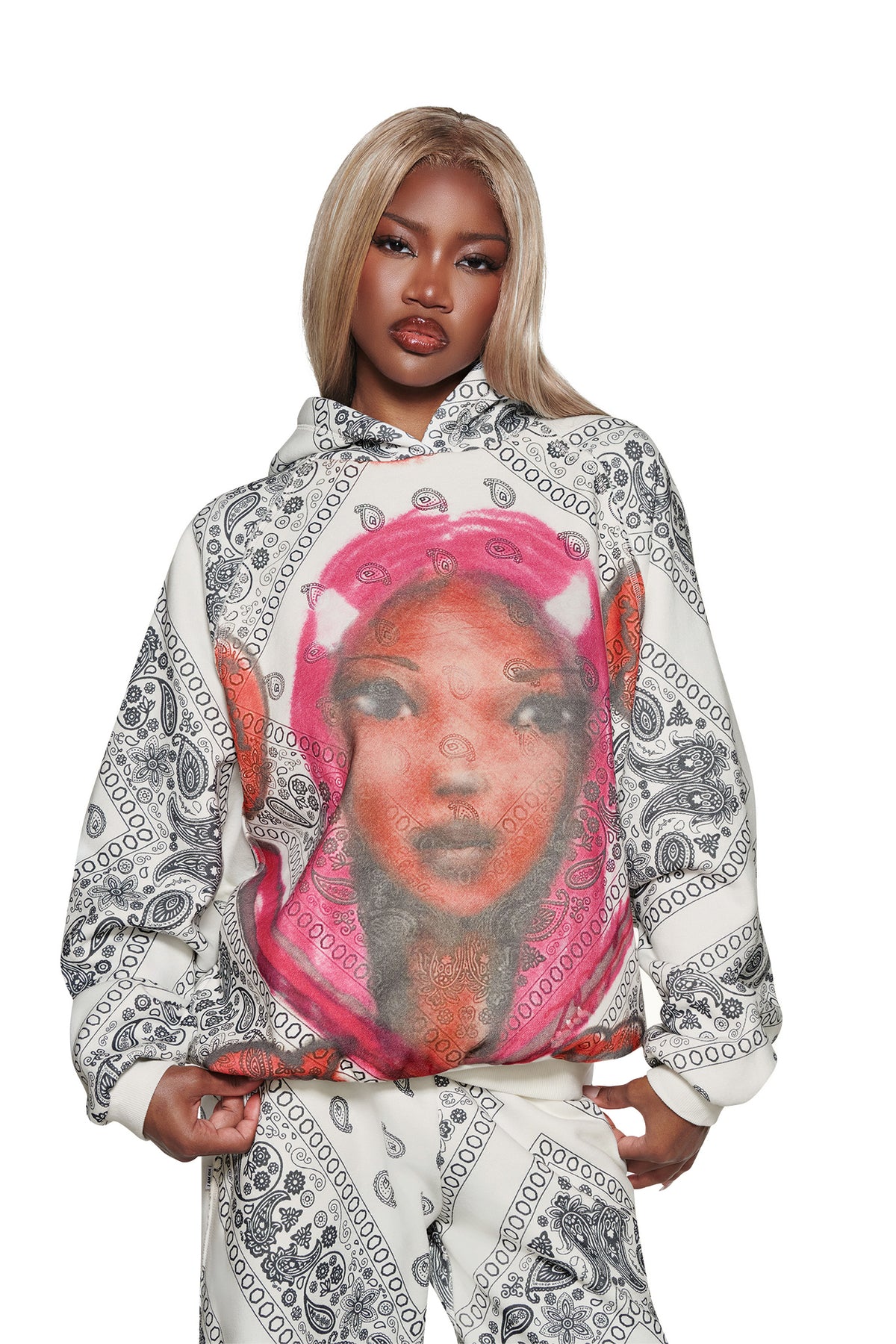 A woman with long blonde hair wears the I.AM.GIA T-REX PULLOVER HOODIE - PAISLEY FACE, featuring black paisley patterns and a colorful graphic of a woman’s face with pink hair, against a white background.