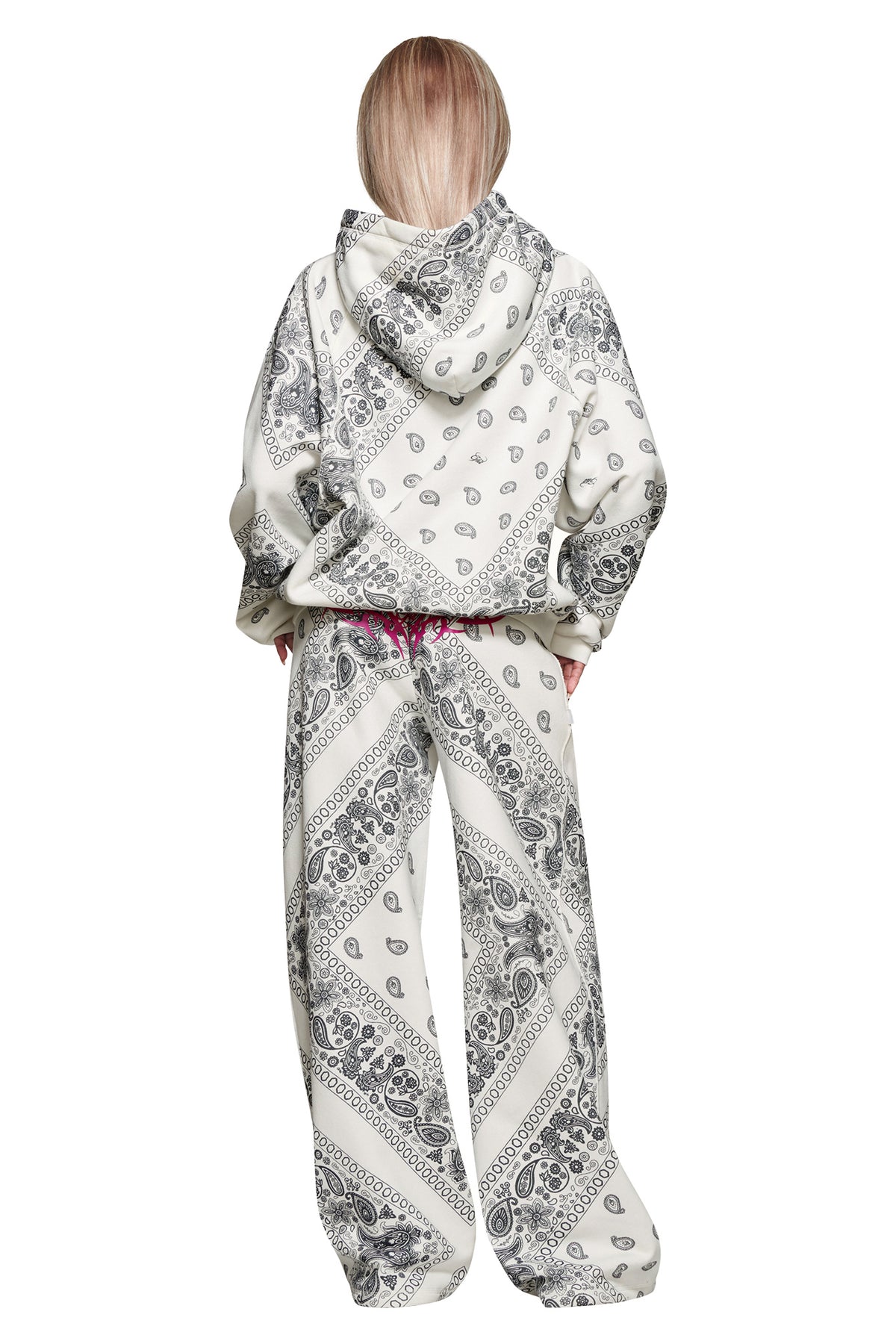 A person with long, straight, light hair is seen from the back wearing the I.AM.GIA T-REX PULLOVER HOODIE - PAISLEY FACE and matching pants, both white with black paisley patterns, against a white background.