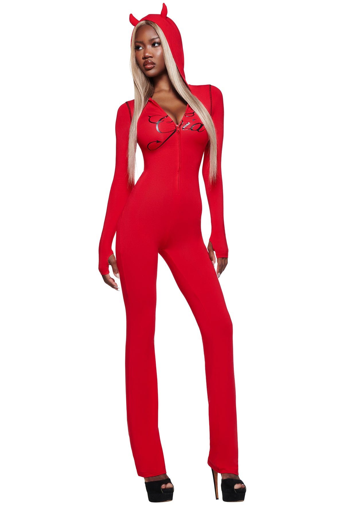 A woman in the I.AM.GIA BLARE HORN JUMPSUIT - RED with a devil horn hood, long blonde hair, and black high heels poses against a white background.
