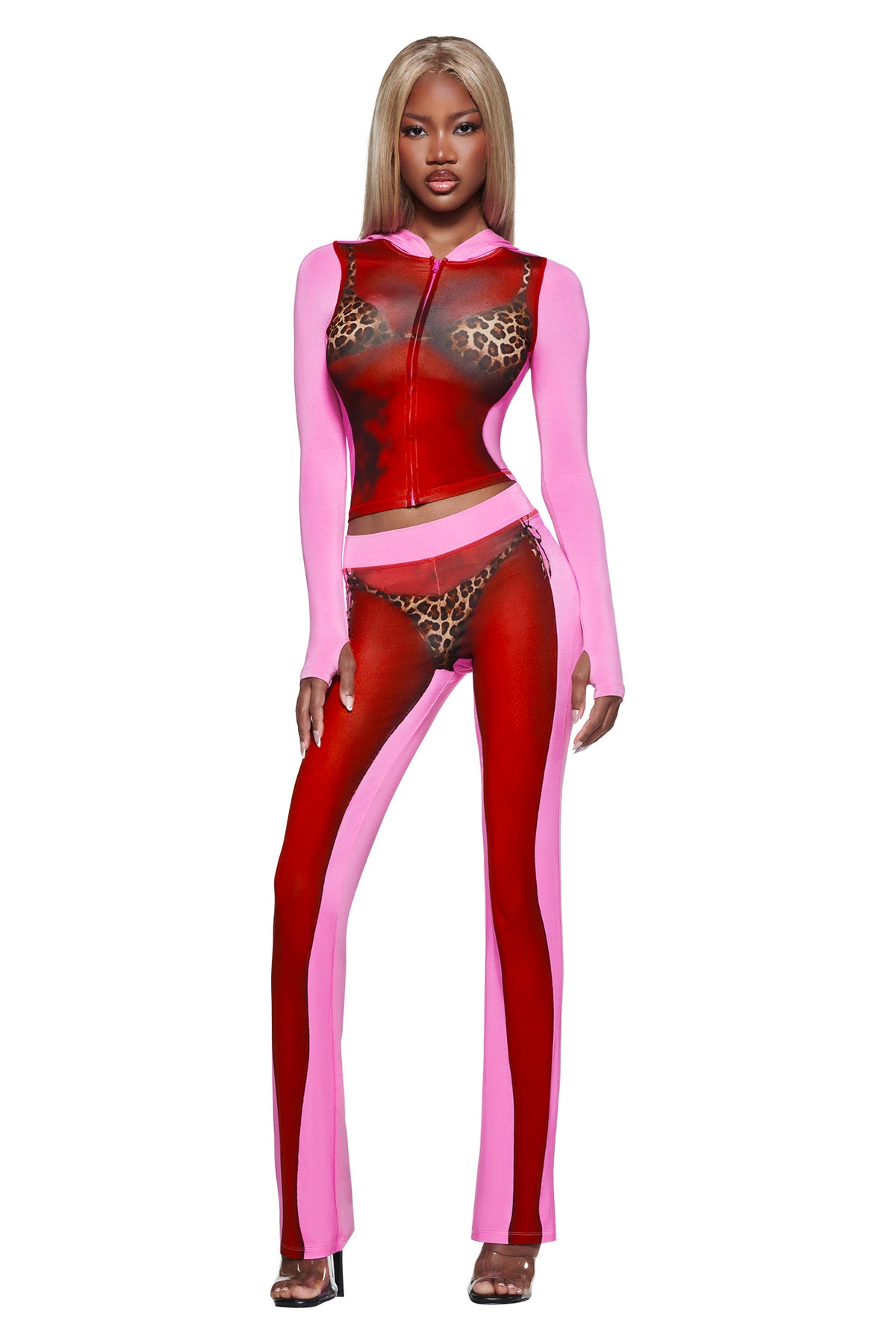 A woman in a pink and red sheer leopard print outfit pairs it with the T-REX SPRAY BODY BLARE TRACKPANT - PINK by I.AM.GIA, perfect for effortless airport style against a white backdrop.