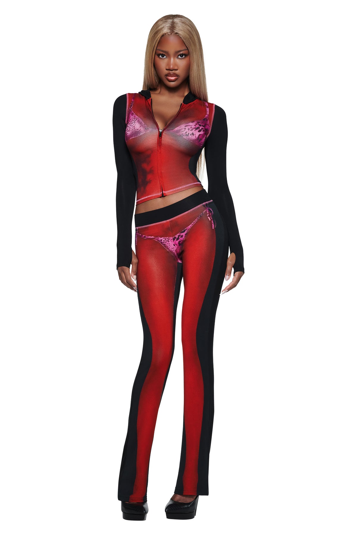 A woman with long blonde hair wears the I.AM.GIA T-REX SPRAY BODY BLARE TRACKPANT - BLACK, a fitted red and black sheer set with faux lingerie print, long sleeves, and matching pants. She stands facing forward against a white background.