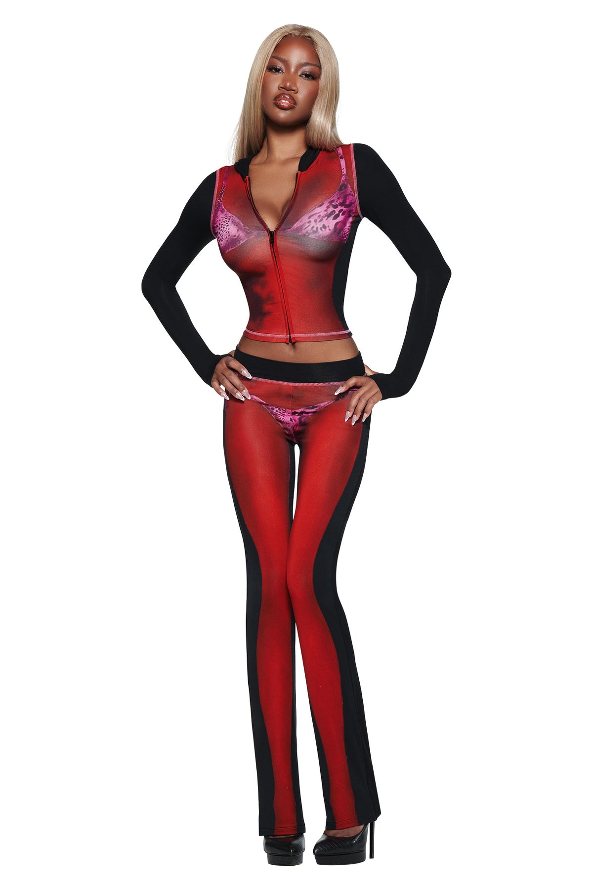 A woman with long blonde hair wears the T-REX SPRAY BODY BLARE TRACKPANT - BLACK by I.AM.GIA, black high heels, and poses with hands on hips against a white background.