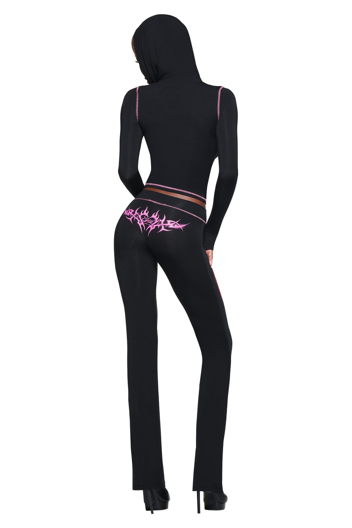 A person in a fitted black hooded outfit with pink details faces away, showcasing high heels—ideal for airport looks or pairing with the I.AM.GIA T-REX SPRAY BODY BLARE TRACKPANT - BLACK.