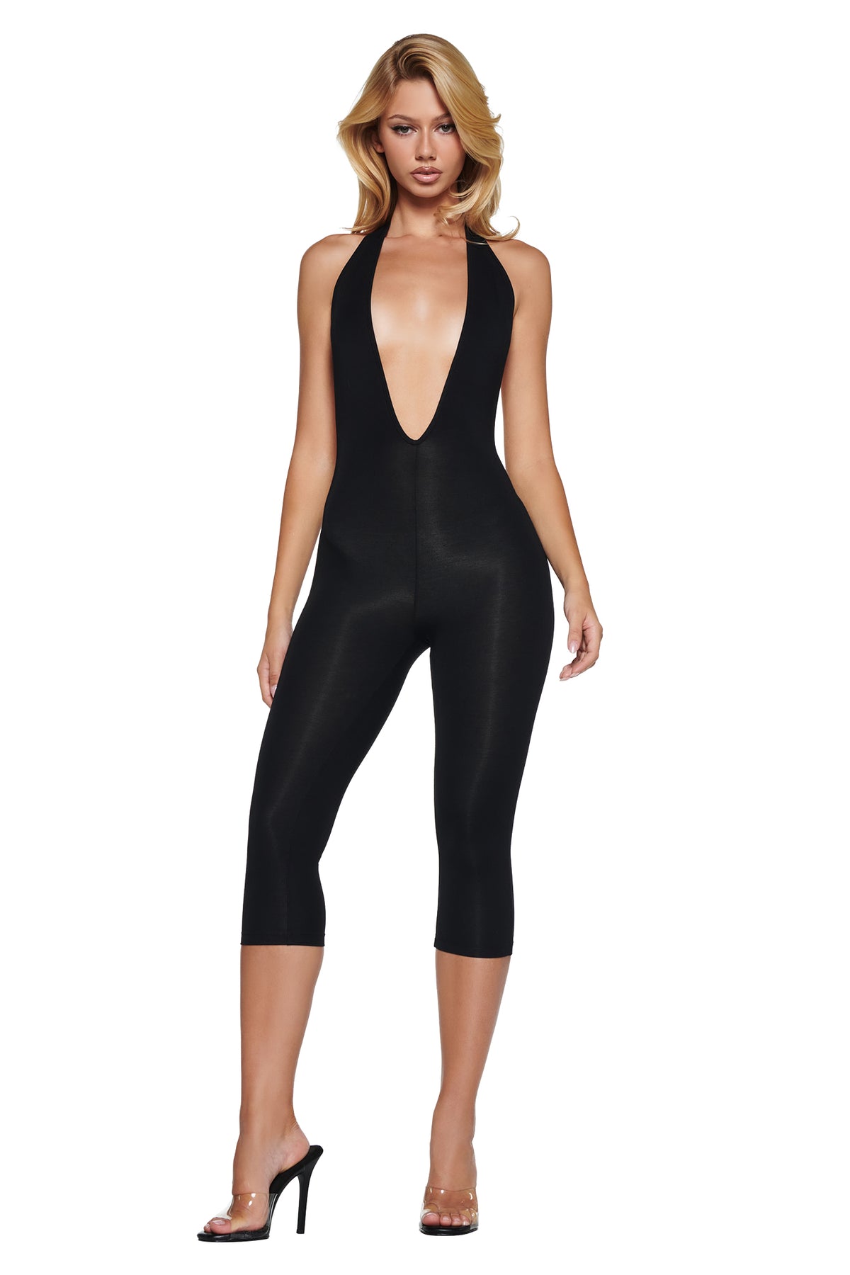 A person wearing a black I.AM.GIA BLARE HALTER CAPRI JUMPSUIT in super-soft fabric, featuring a deep plunge neckline and clear high-heeled sandals.