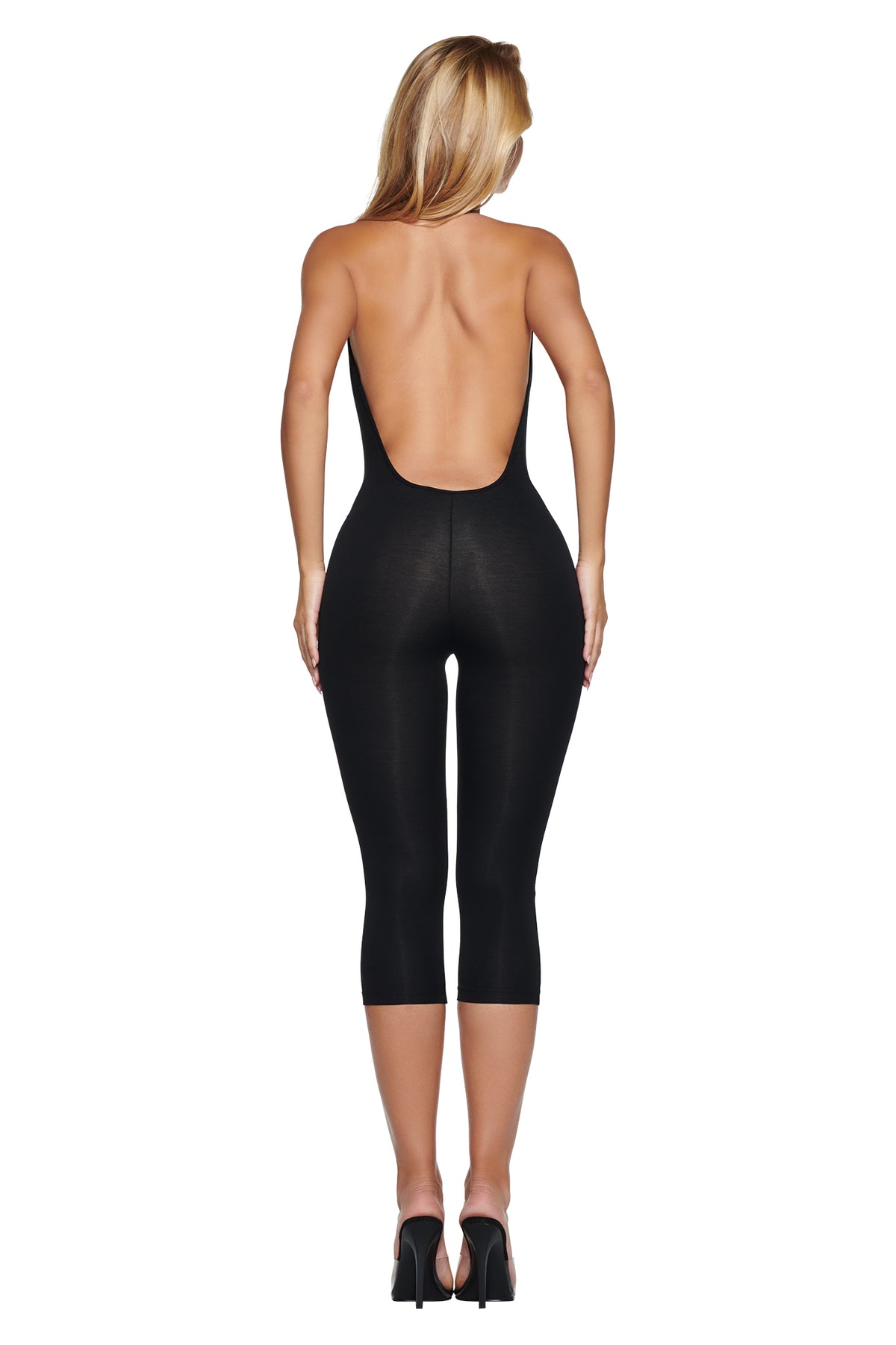 A woman viewed from behind, wearing a black BLARE HALTER CAPRI JUMPSUIT in super-soft fabric with capri-length legs and high-heeled sandals.