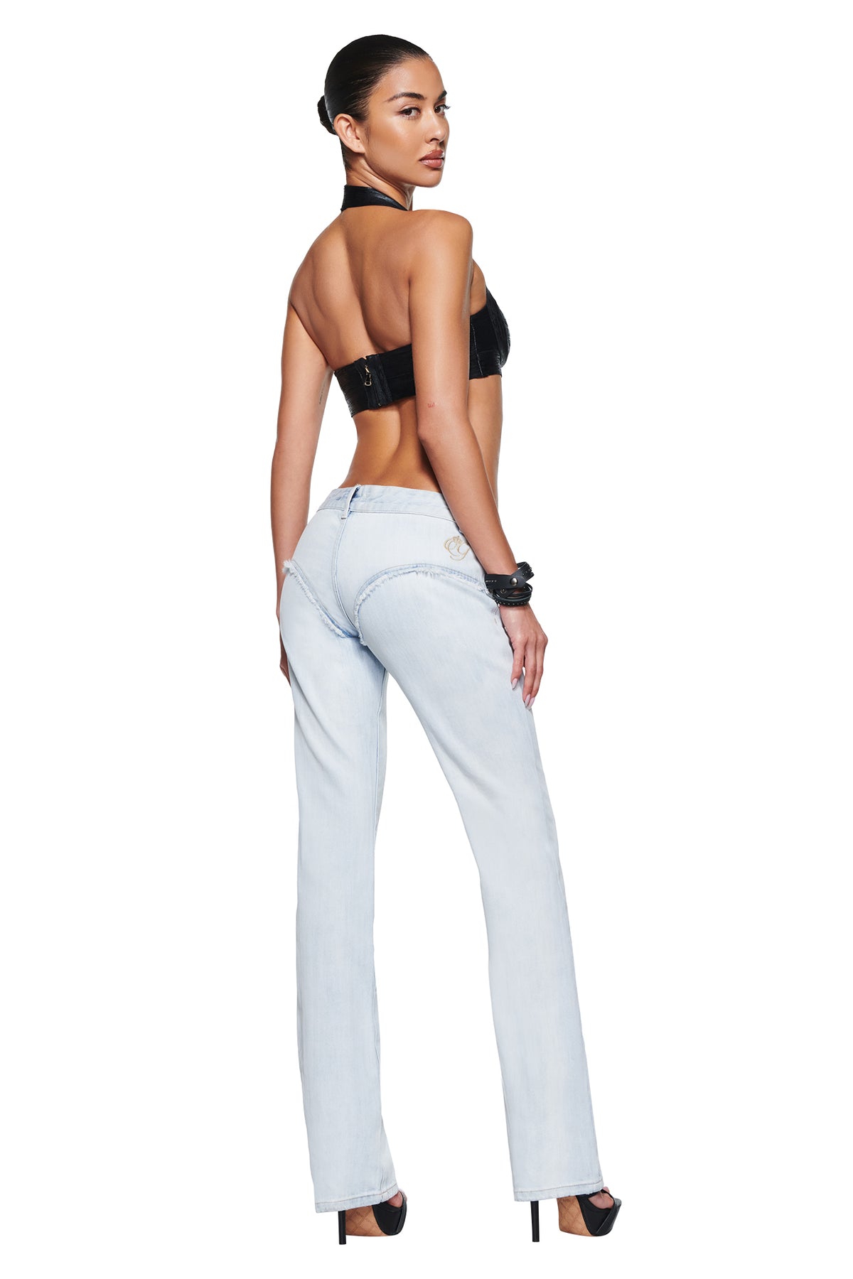 A person stands with their back to the camera, wearing I.AM.GIA FERN JEAN - LIGHT DENIM with a low-rise fit and a black halter top.