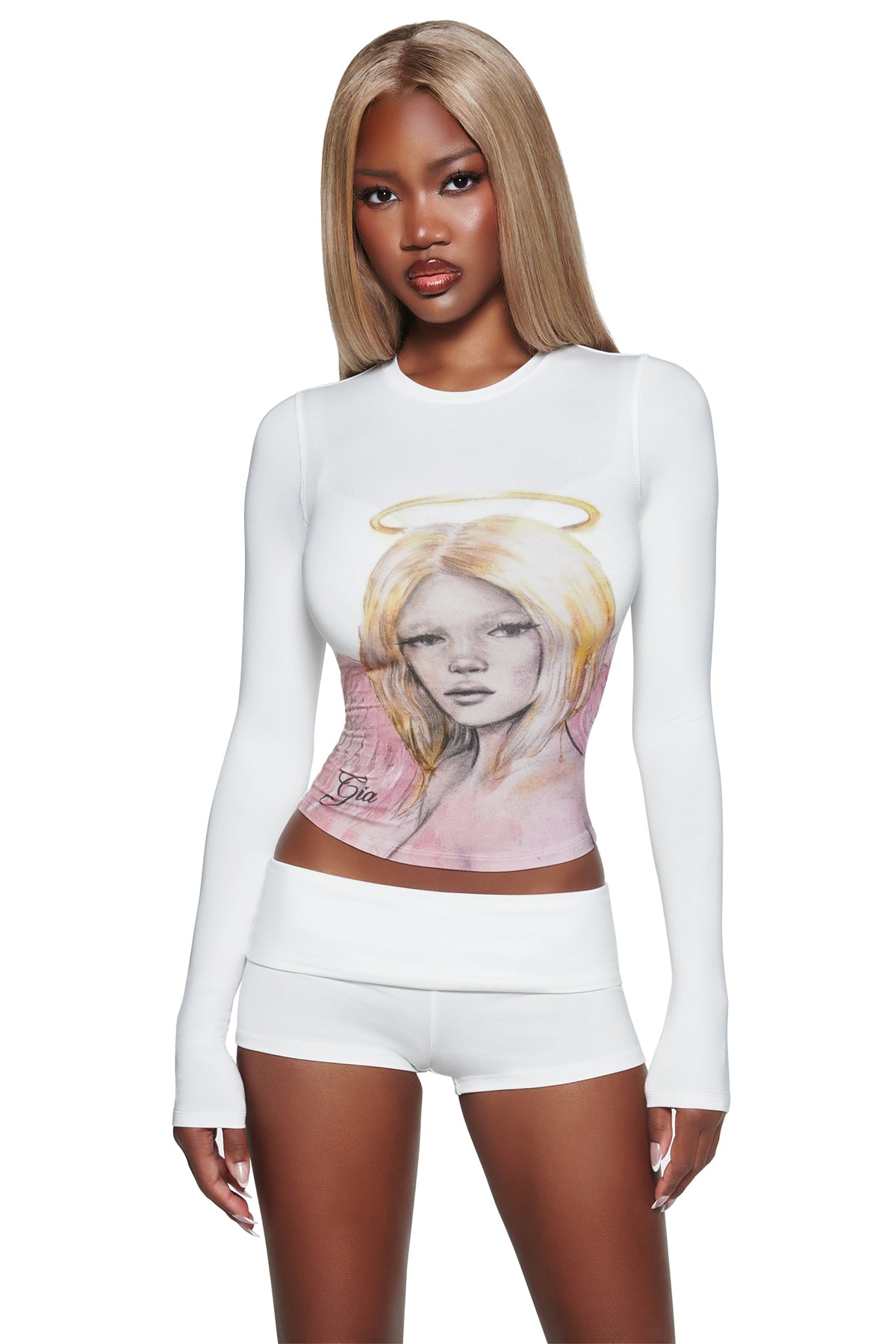 A woman with long straight blonde hair wears a white long-sleeve crop top with an angel graphic and the I.AM.GIA T-REX BLARE 2.0 SHORT - WHITE, standing against a white background.
