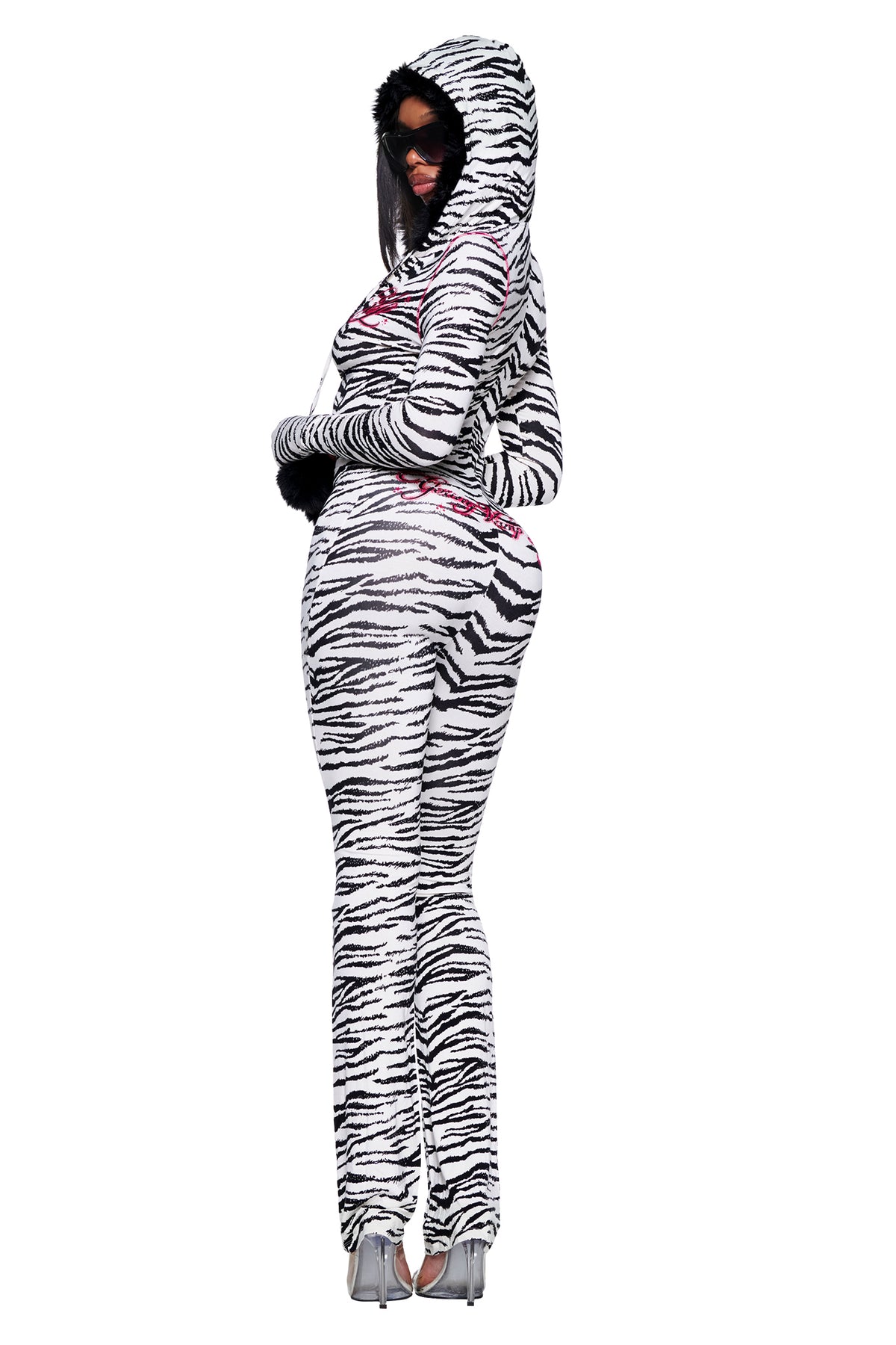 A person wearing a hooded YVL BLARE FUR LINED JUMPSUIT - ZEBRA with black faux fur trim at the hood and cuffs, featuring red graphic text on the chest and back.