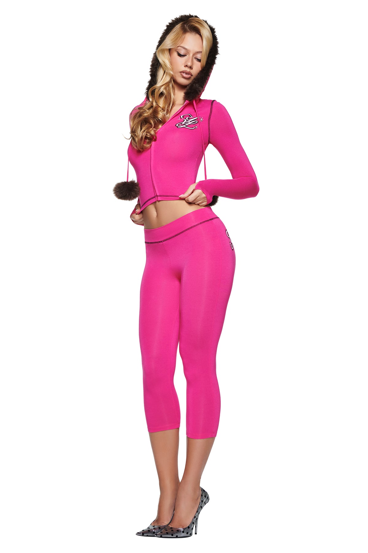 A woman wears a bright pink I.AM.GIA YVL BLARE FUR LINED HOODIE with a fur-trimmed hood and matching cropped leggings from the Young Vamp Life collaboration.