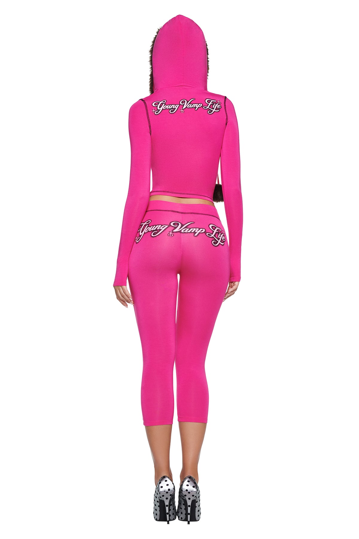 A person wearing a bright pink YVL BLARE FUR LINED HOODIE and matching cropped leggings, both featuring “Young Vamp Life” in cursive script across the back.