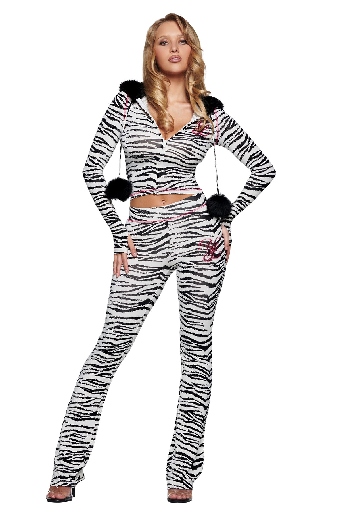 A woman wears a long-sleeved, cropped, zippered hoodie and matching zebra-print YVL BLARE TRACKPANT - ZEBRA, both featuring black fur pom-pom ties.