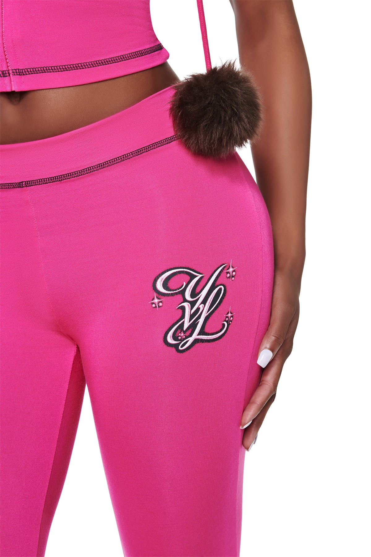 Hot pink I.AM.GIA YVL BLARE CAPRI - PINK leggings crafted from bamboo fabrication, featuring a decorative “YL” emblem on the hip and a fluffy pom-pom attached to the waistband.