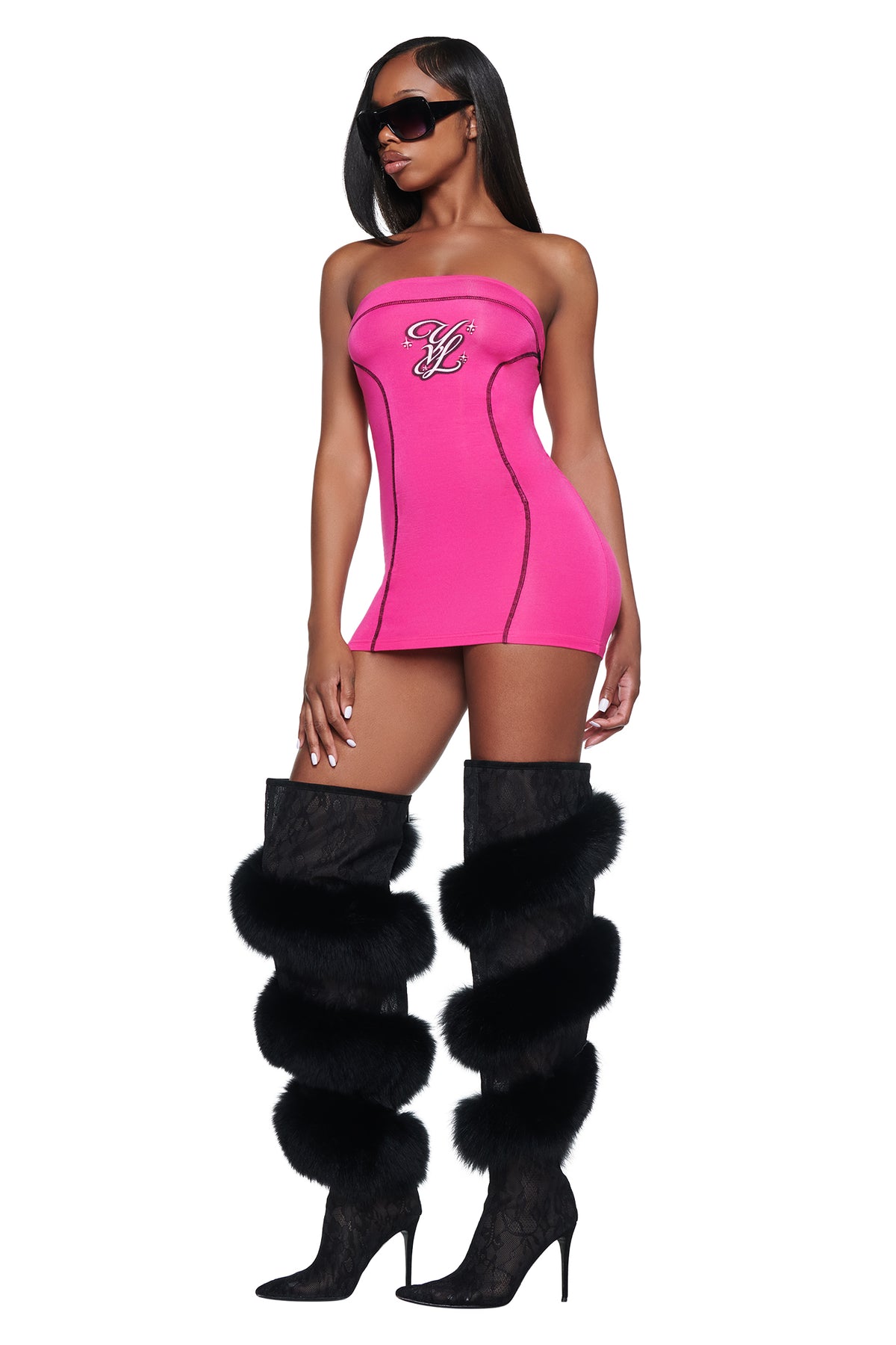 A woman wearing a hot pink I.AM.GIA YVL BLARE TUBE MINI DRESS - PINK with black trim and black lace-up thigh-high boots with fur trim.