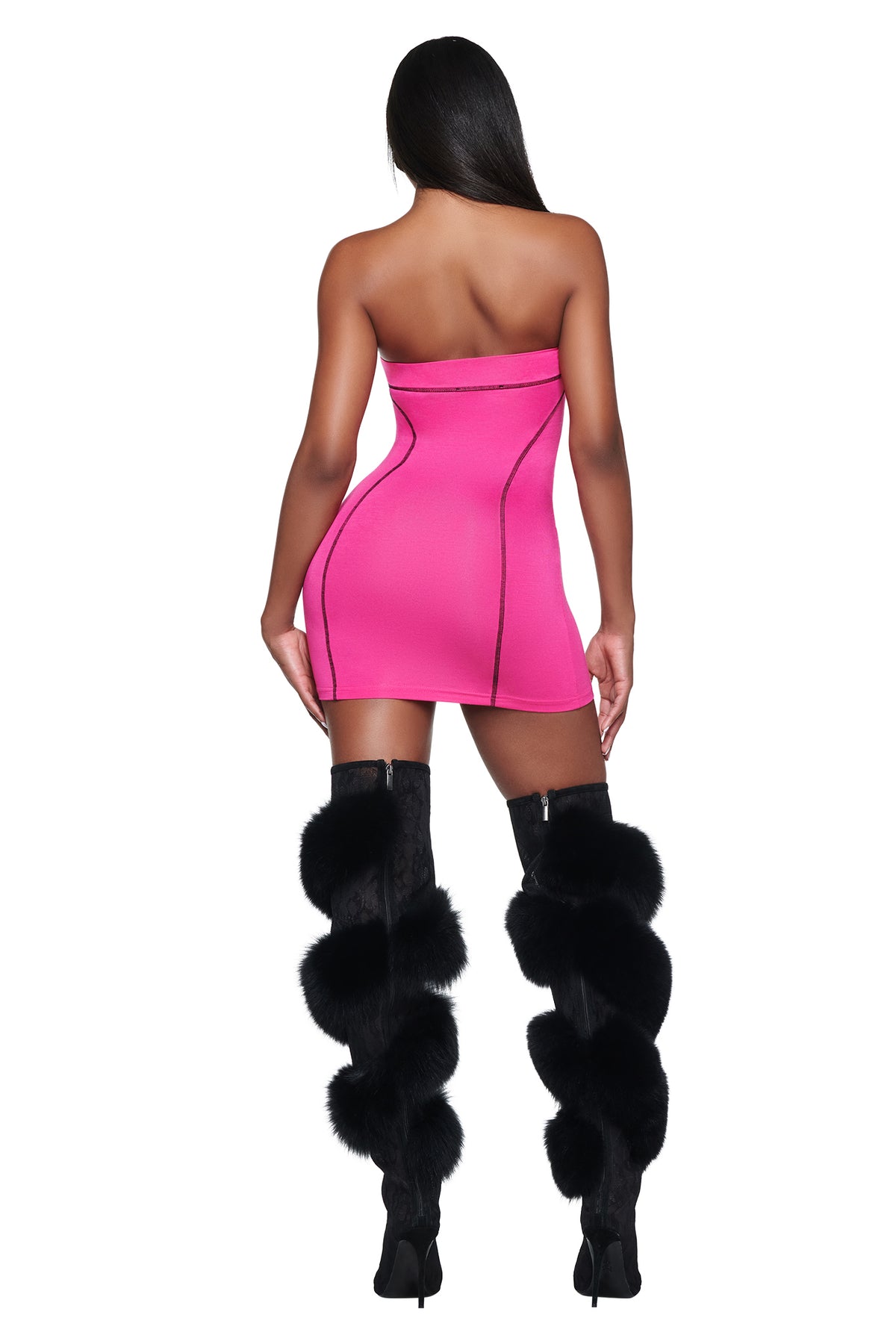A person seen from behind wearing a hot pink I.AM.GIA YVL BLARE TUBE MINI DRESS with exposed black seams and thigh-high black boots adorned with large fur pom-poms.