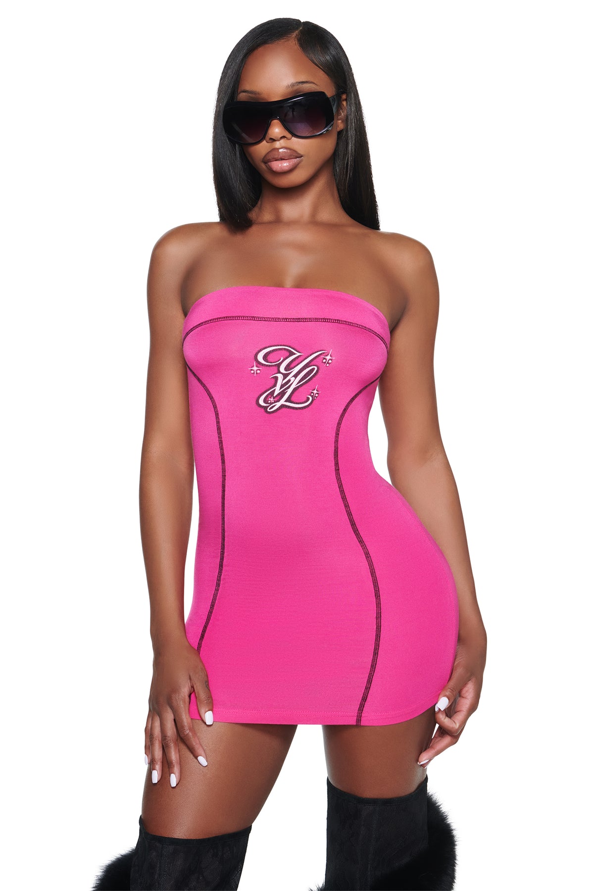 A person wears a hot pink YVL BLARE TUBE MINI DRESS - PINK with black seam detailing and a decorative logo on the chest, paired with oversized sunglasses.