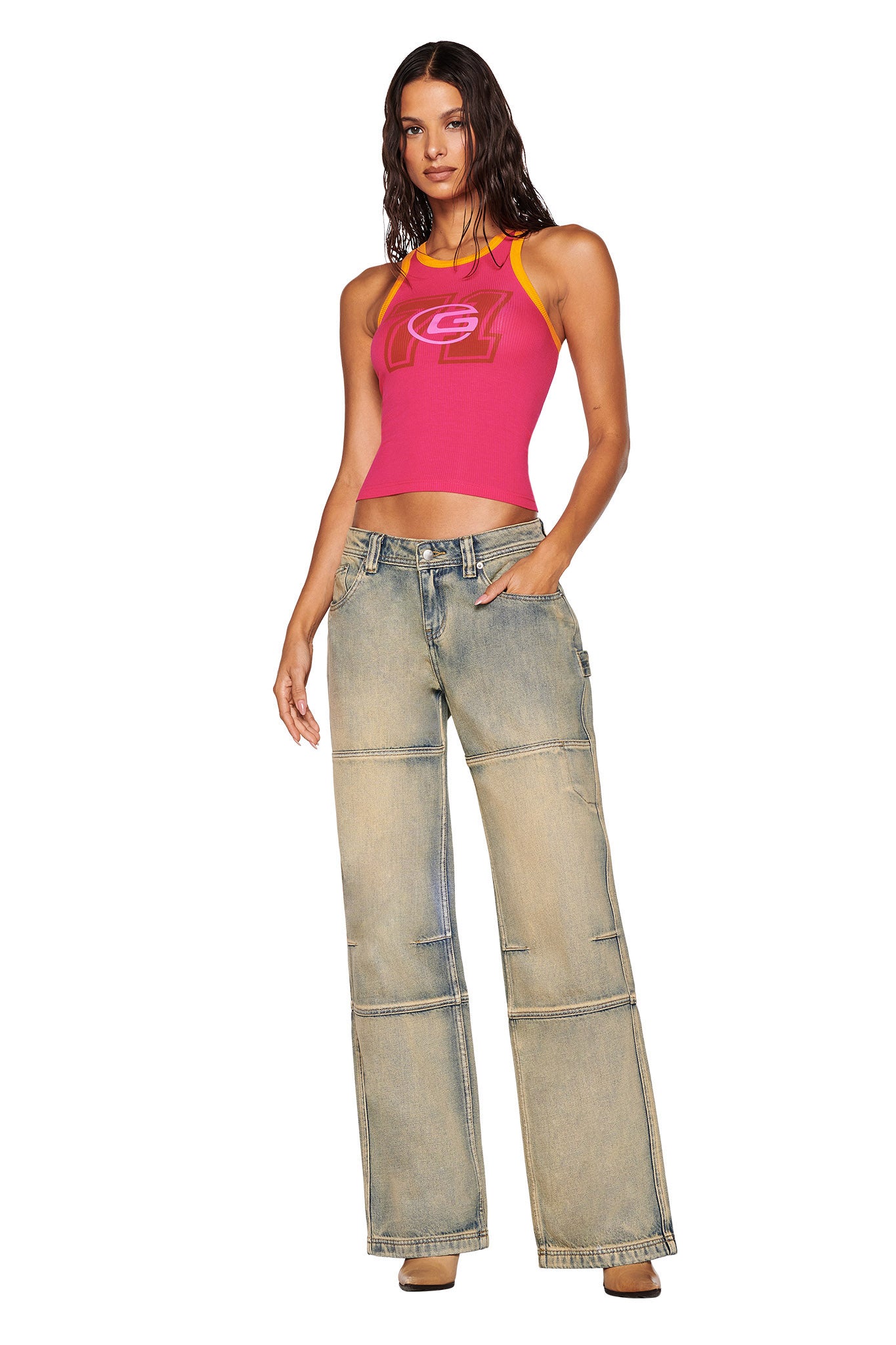 A person wearing a hot pink I.AM.GIA PENELOPE TANK featuring a custom graphic and loose-fitting, light blue jeans. They have long hair and are standing against a plain white background, with one hand in their pocket.