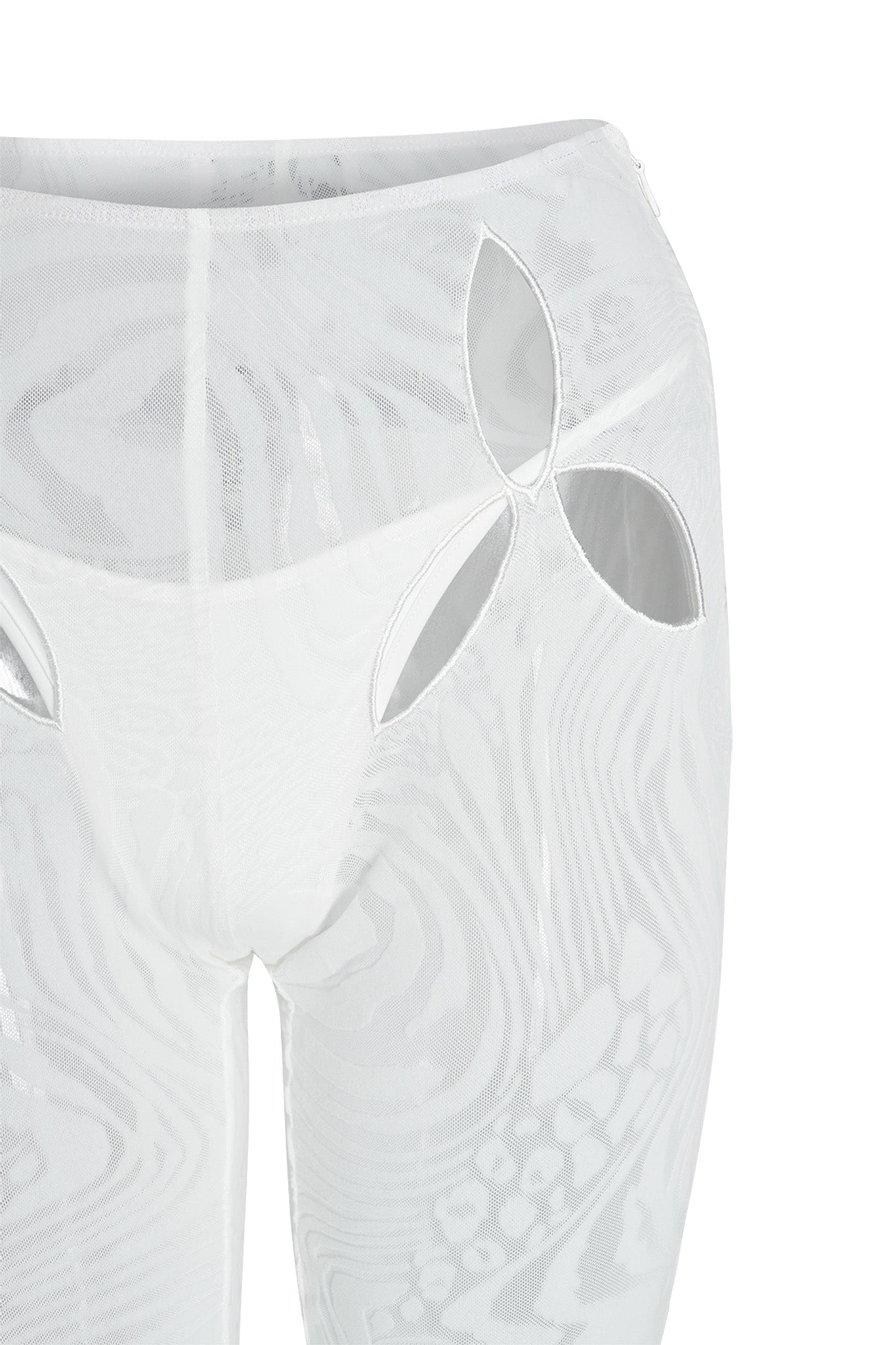 Close-up of the I.AM.GIA AMINA PANT - WHITE featuring a floral cut-out design on the right upper thigh. These mid-high rise, white sheer mesh pants showcase intricate swirling patterns throughout, adding to their delicate and sophisticated appearance. The white background highlights the elaborate burnout velvet print details.