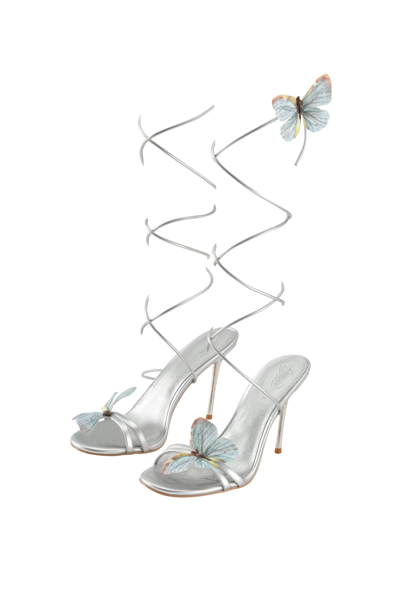 The SCARLETTE HEEL - SILVER by I.AM.GIA features silver metallic strappy heels with open toes, ankle wrap straps, and blue butterfly appliques on the toes and straps.