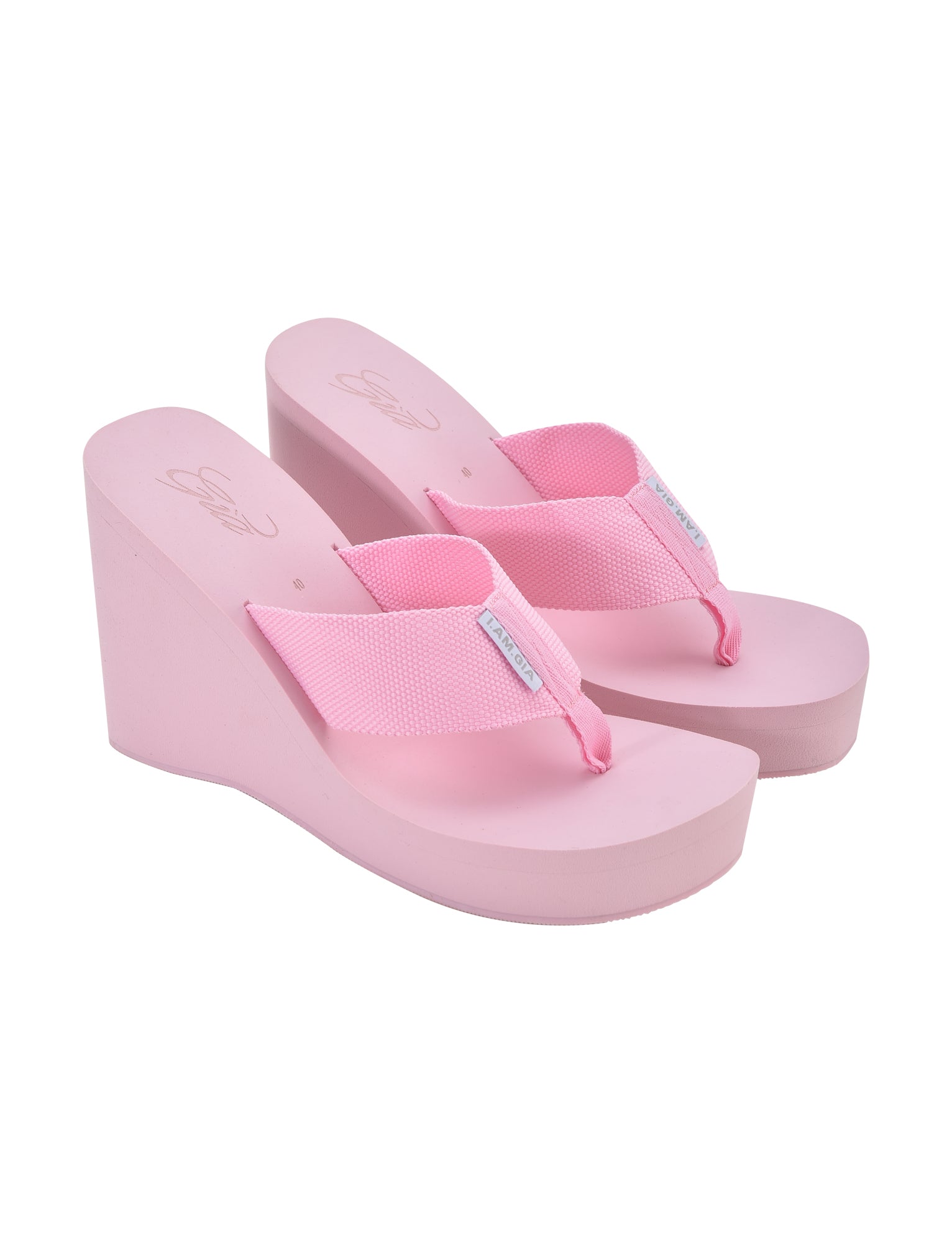 A pair of I.AM.GIA SHELBY FLIP FLOP in baby pink, featuring thick straps and elevated heels. The soles and straps are both pink, providing a casual and comfortable design perfect for warm weather.